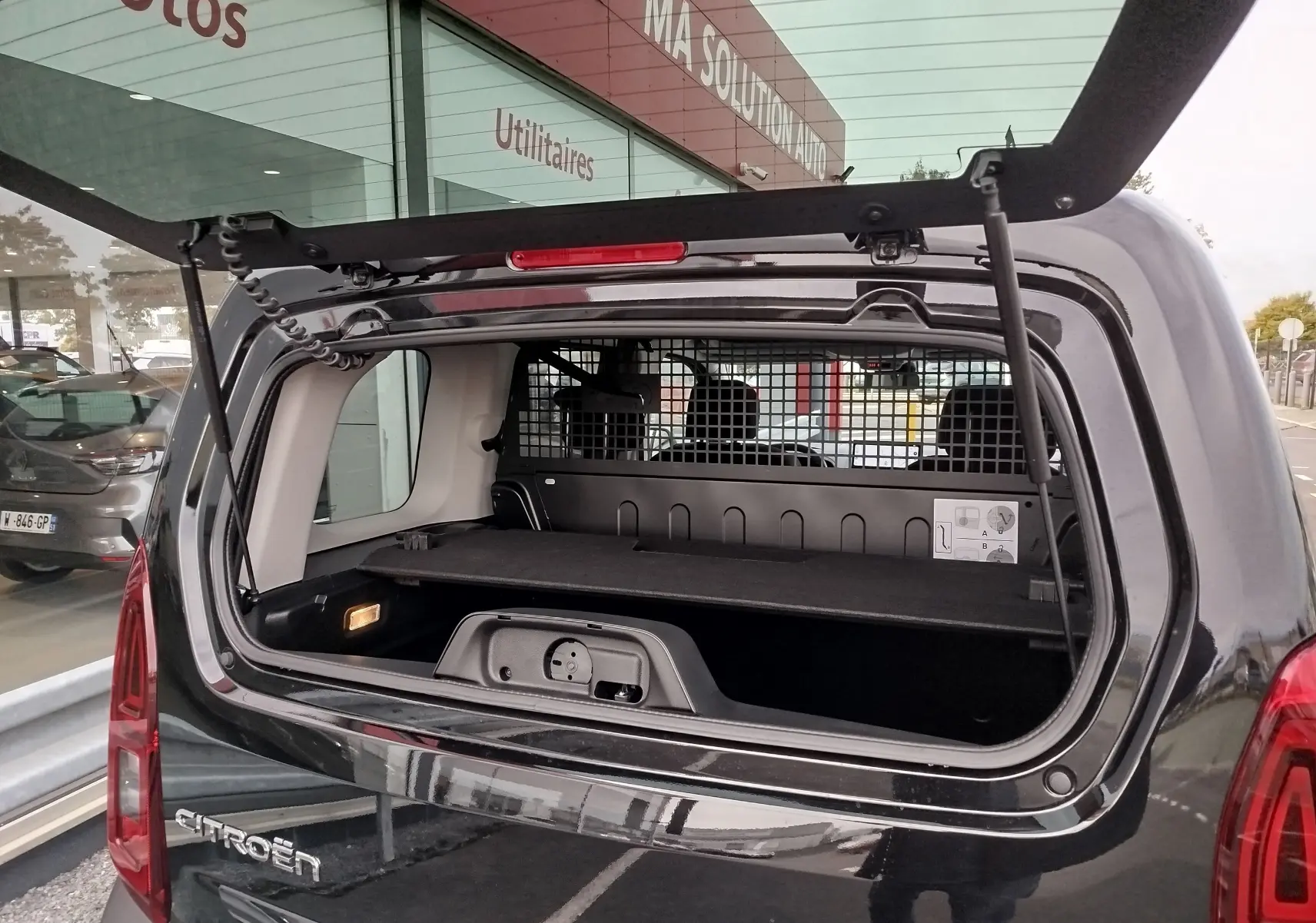 Vue arrière du Citroën Berlingo noir Perla Nera 2025 avec hayon ouvert et séparation grillagée visible dans le coffre.