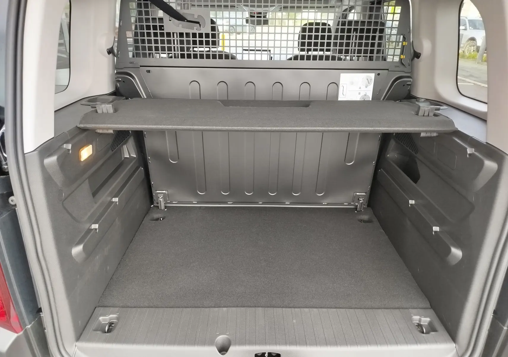Coffre ouvert vu de l'arrière d'un Citroën Berlingo noir Perla Nera, avec séparation grillagée et tablette de rangement.