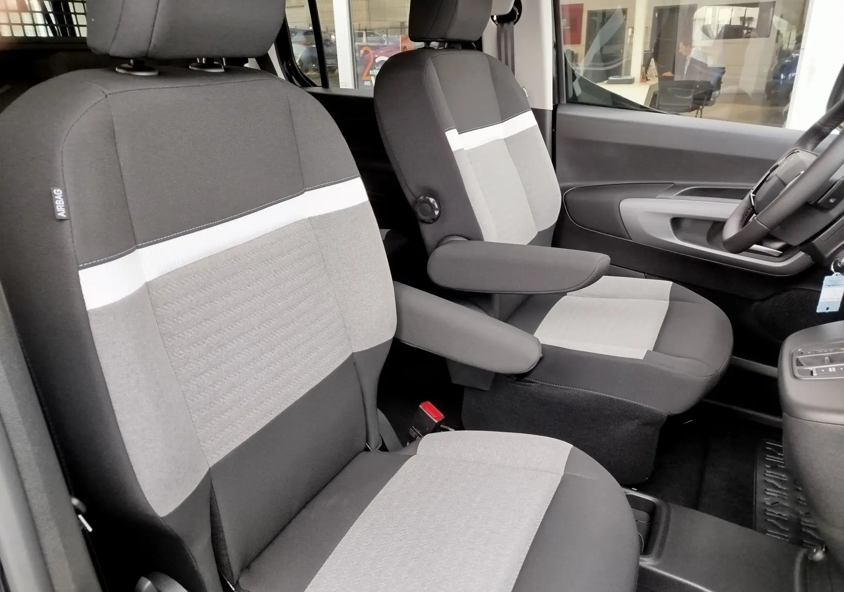 Vue intérieure des sièges avant gris et noir du Citroën Berlingo 2025, avec accoudoirs et détails tissu contrastés.