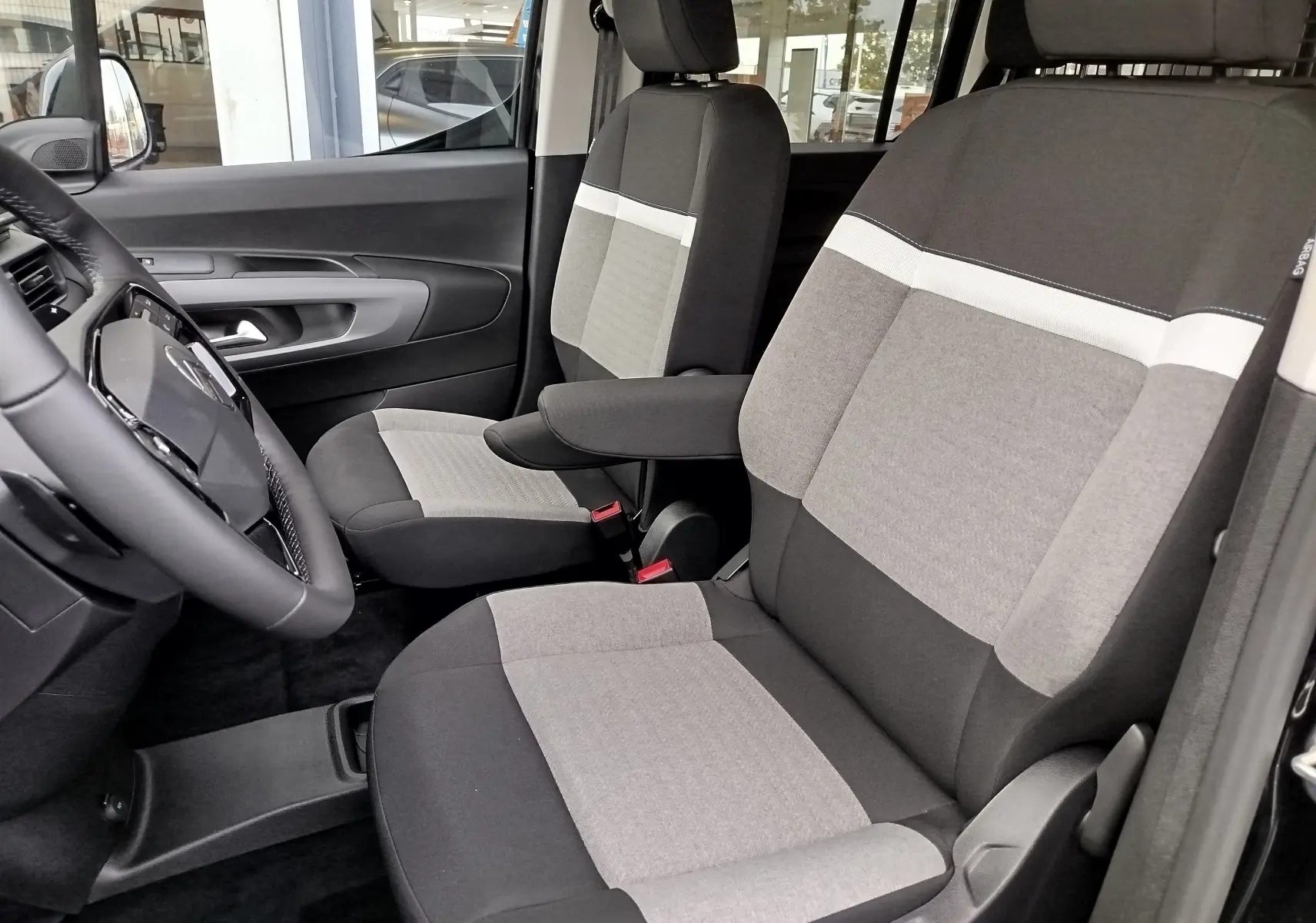 Intérieur du Citroën Berlingo 2025, vue côté gauche sur les sièges avant gris et noir avec accoudoir central.