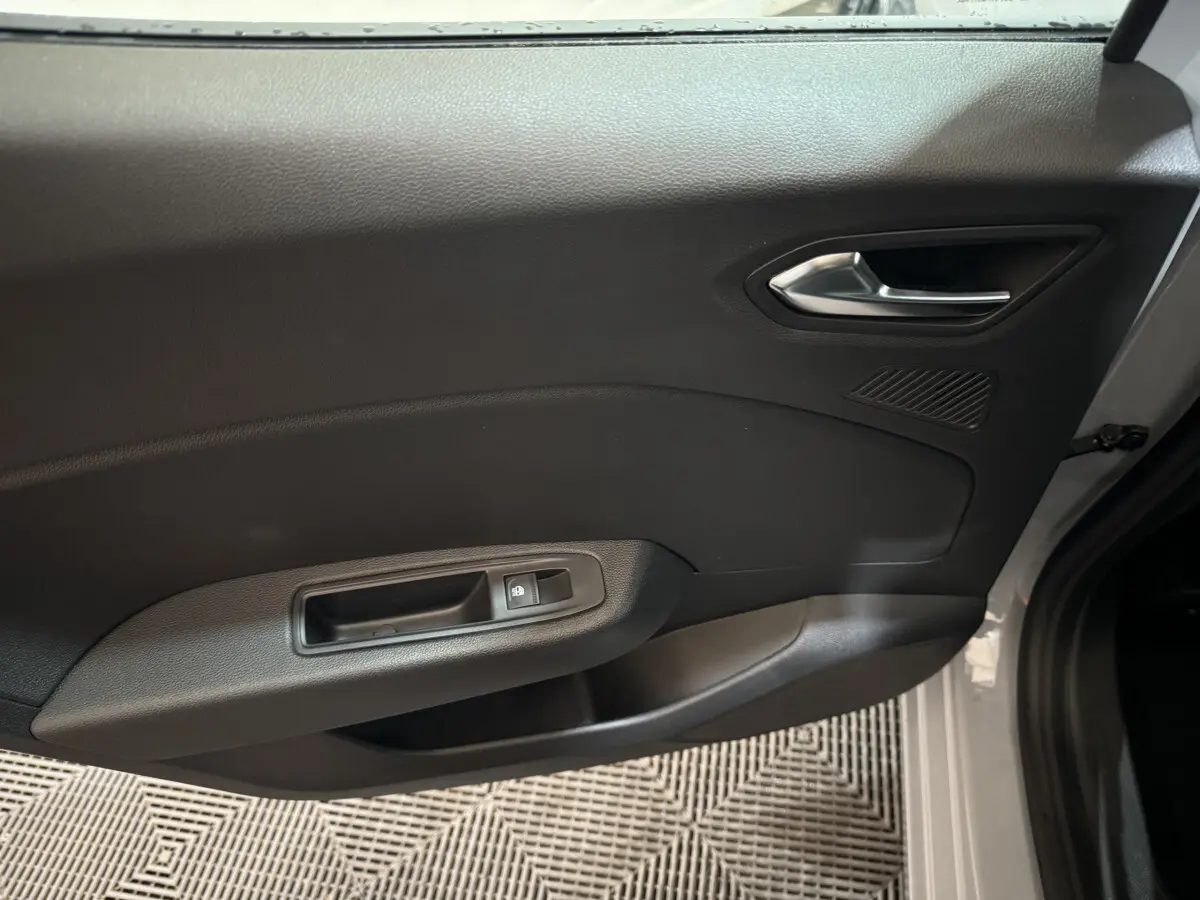 Vue intérieure de la porte côté droit gris foncé de la Renault Clio 2025 avec poignée métallique et commande de vitre électrique.