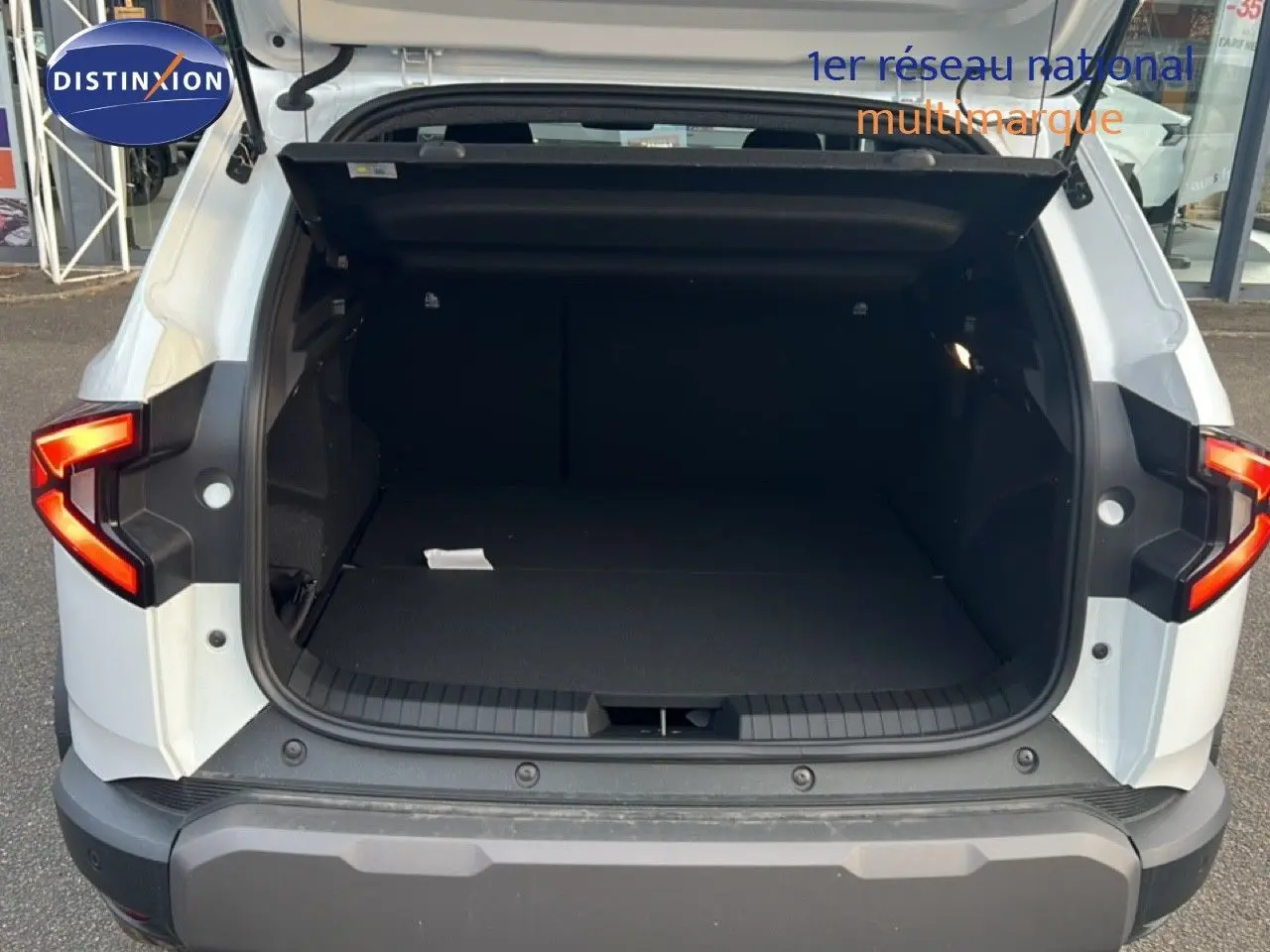 Vue arrière du Dacia Duster blanc glacier 2025 avec coffre ouvert et feux arrière allumés.