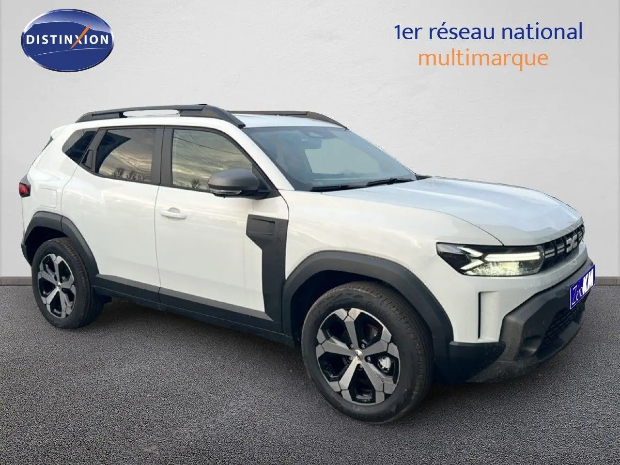 SUV Dacia Duster blanc glacier en 3/4 avant droit, avec jantes bi-ton et barres de toit noires.