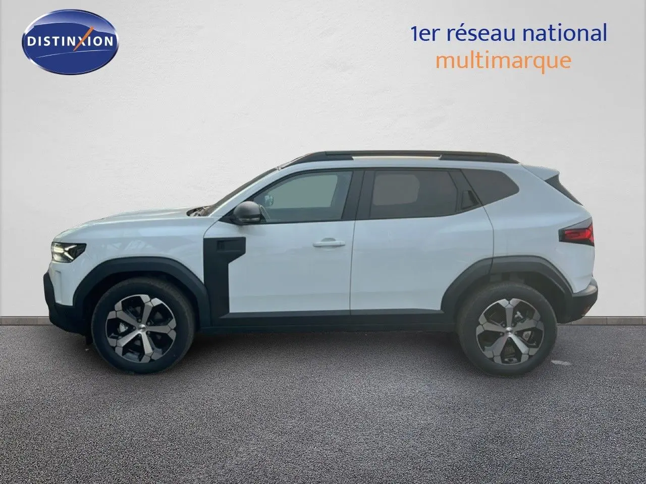 Vue de profil droit du Dacia Duster 1.6 Hybrid blanc glacier avec jantes bi-ton et protections noires contrastées.