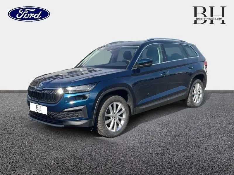 Vue 3/4 avant droite d'un Skoda Kodiaq 2023 bleu lave métallisé avec jantes alu et barres de toit.