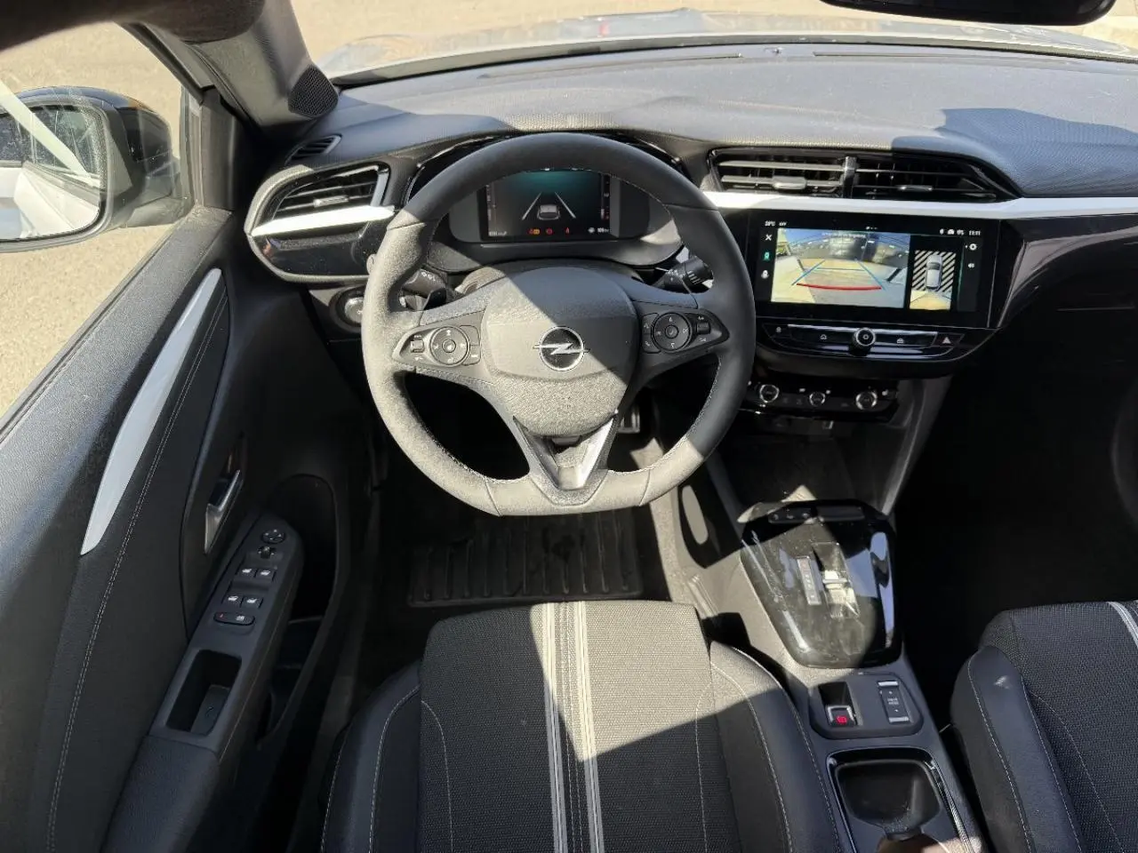 Vue intérieure de l’Opel Corsa 1,2 Hybrid 2025, volant multifonction, écran tactile avec caméra de recul, sièges tissu noir.