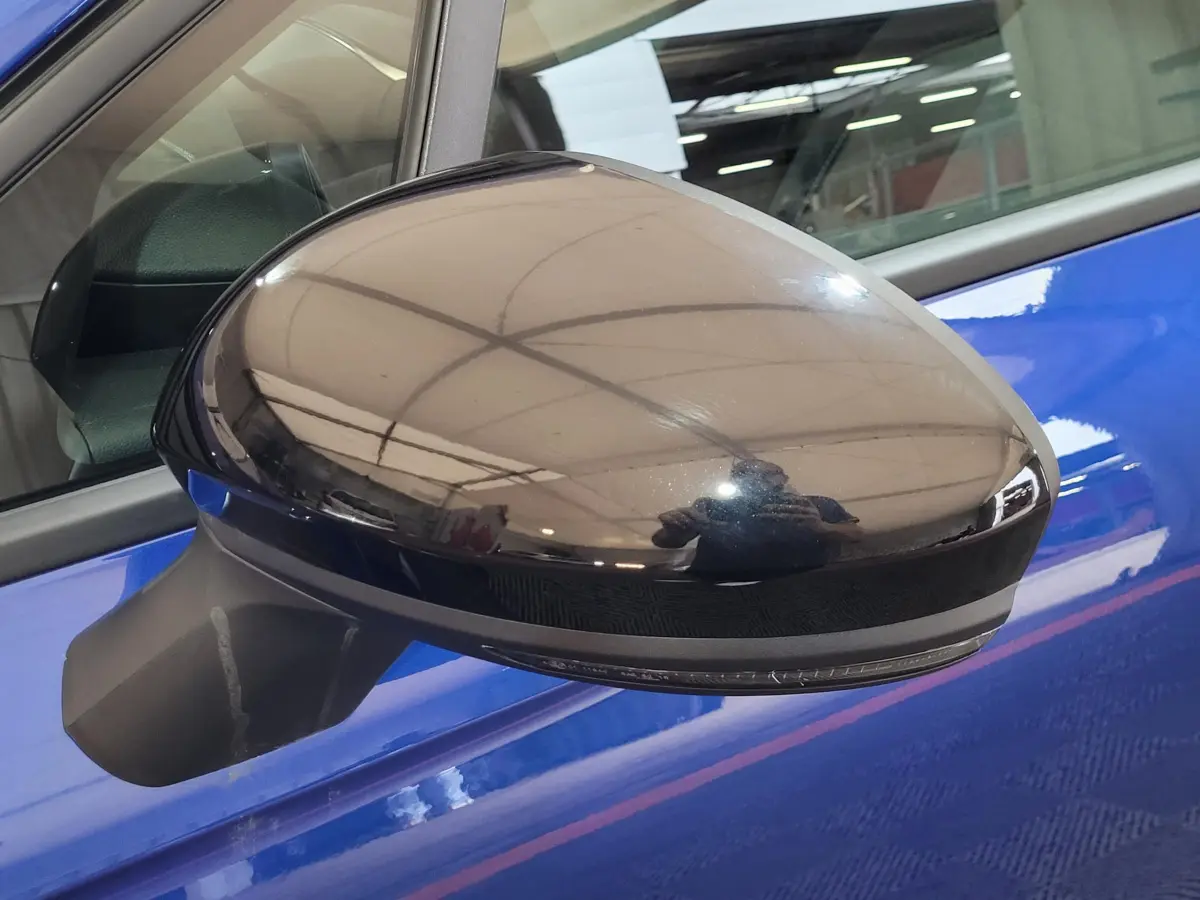 Rétroviseur extérieur noir côté conducteur sur Renault Clio bleu, avec surface brillante reflétant l'environnement intérieur.
