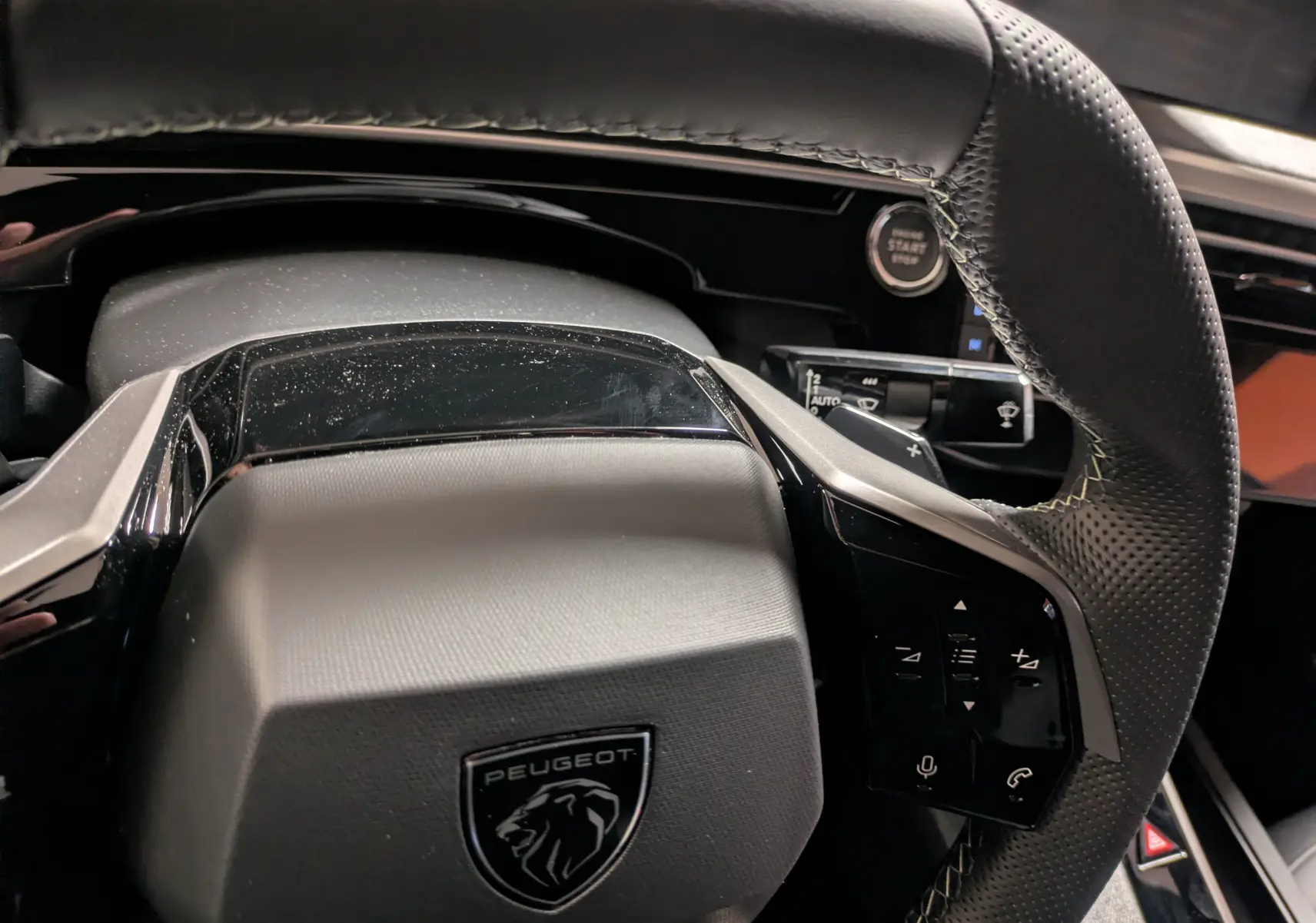 Gros plan sur le volant noir perforé du Peugeot 3008 Hybrid 145 GT avec commandes intégrées et bouton Start/Stop visible.