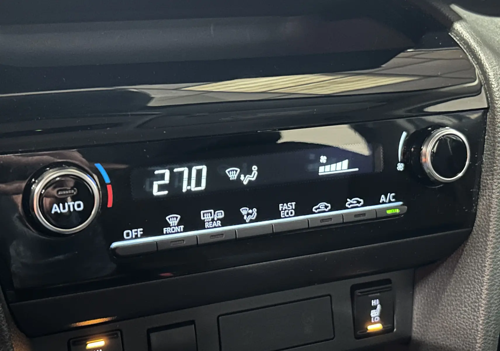 Détail de la console de climatisation digitale de la Toyota Yaris Cross 2025 gris minéral, avec réglage à 27°C et sièges chauffants activés.