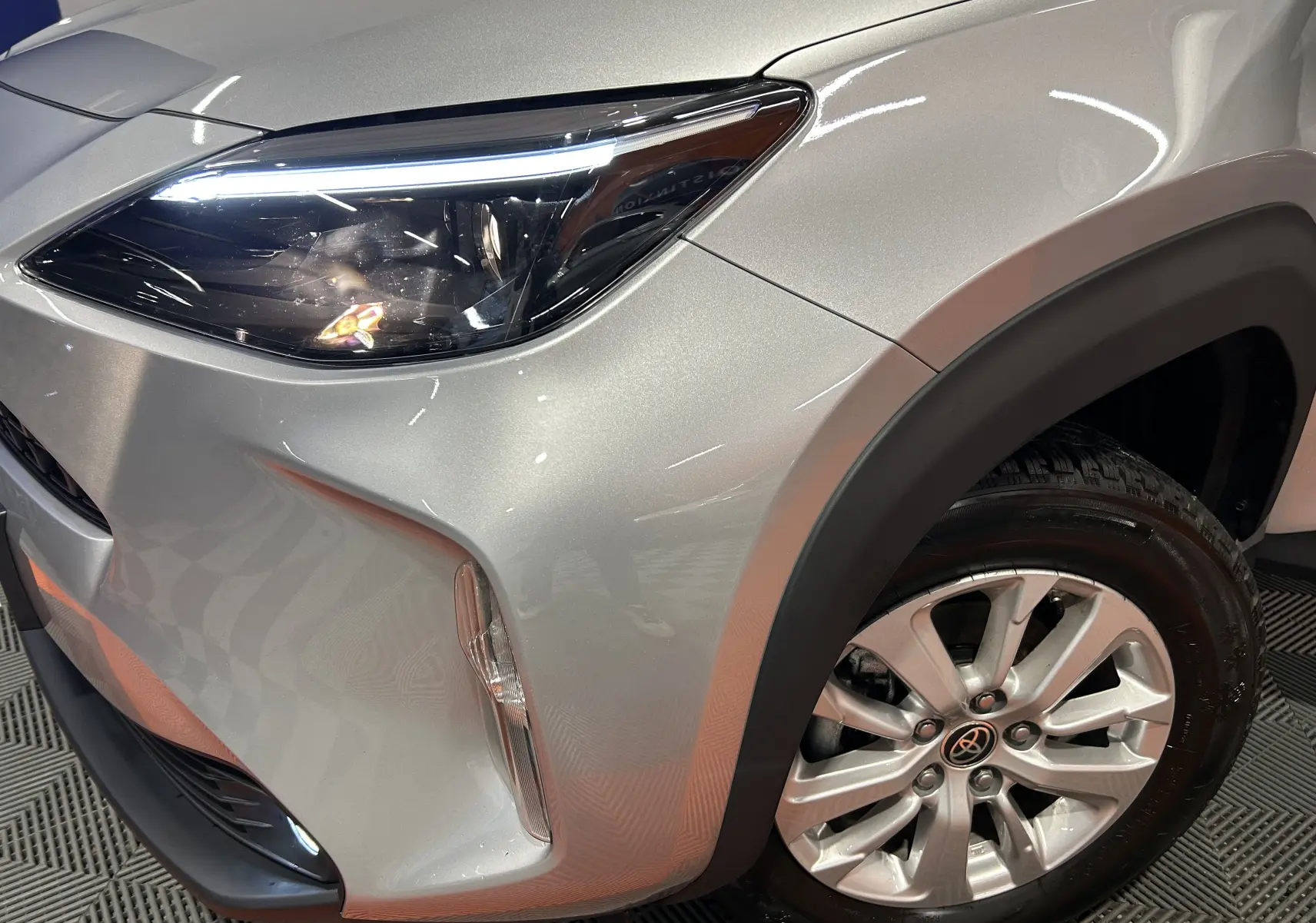 Gros plan sur l'avant droit gris minéral de la Toyota Yaris Cross 2025, mettant en valeur le phare LED et la roue alu.