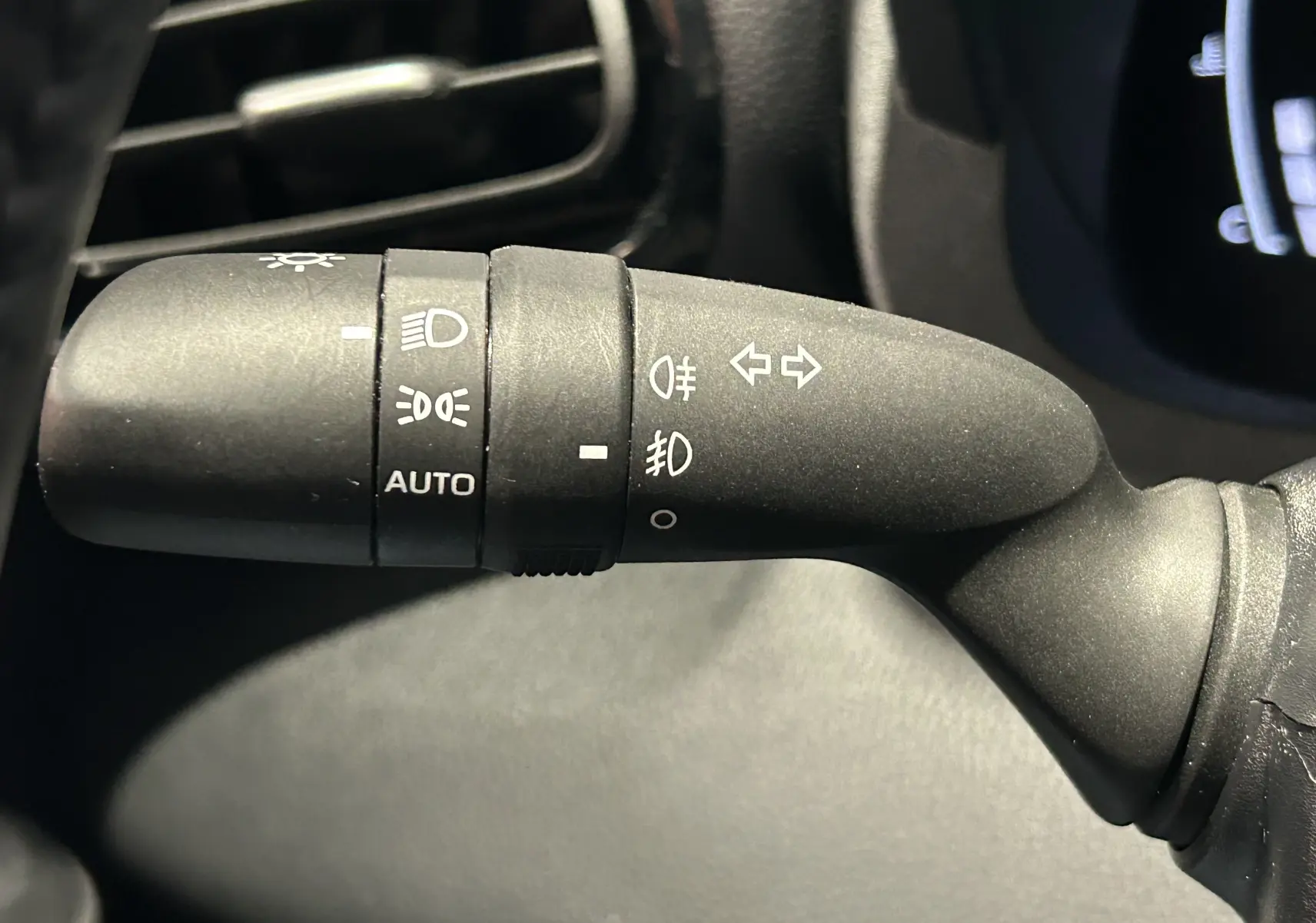 Gros plan sur la commande des phares et clignotants du Toyota Yaris Cross gris minéral, intérieur noir.