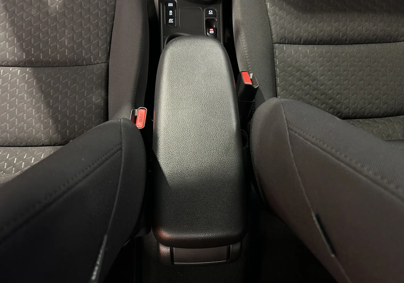 Vue plongeante sur l'accoudoir central noir et les sièges en tissu gris foncé de la Toyota Yaris Cross 116h Active MC24.