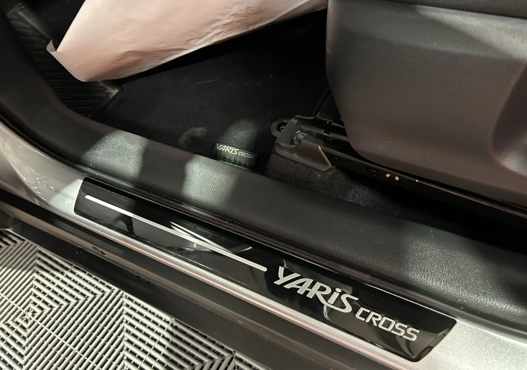 Gros plan sur la plaque de seuil de porte et le tapis noir avec logo Yaris Cross, intérieur gris minéral visible.