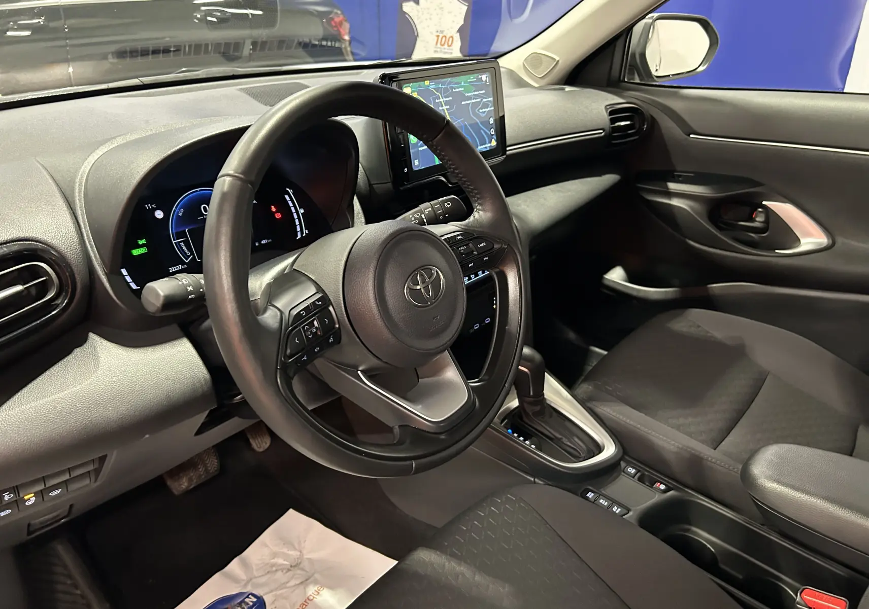 Vue intérieure côté conducteur de la Toyota Yaris Cross 116h Active 2025, avec volant cuir et écran tactile central.