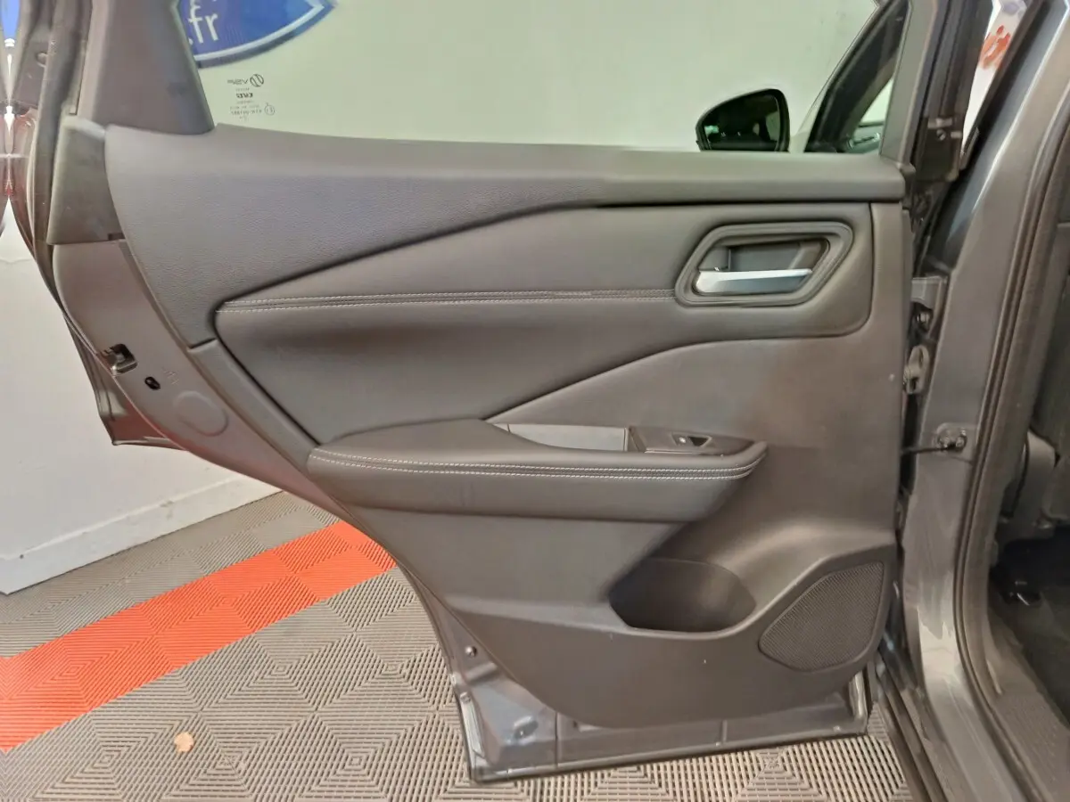 Vue intérieure de la porte arrière gauche gris foncé du Nissan Qashqai 1.3 MHEV 2022 avec accoudoir et commande de vitre.
