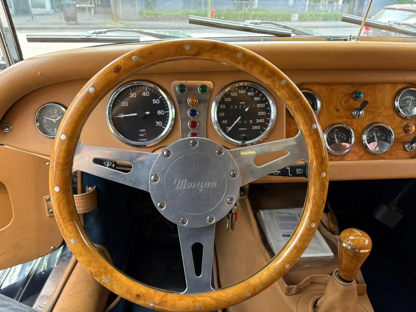 Vue intérieure centrée sur le volant en bois et le tableau de bord en bois clair d'une Morgan Plus 4 bleu foncé de 1995.