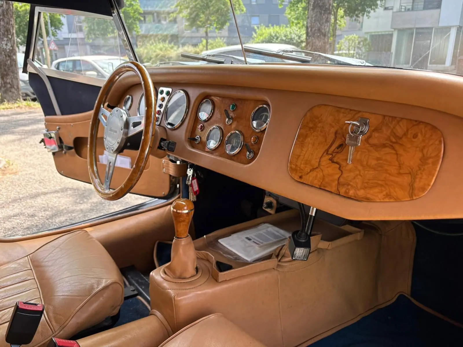 Intérieur beige de la Morgan Plus 4 1995, vue côté conducteur sur tableau de bord en bois et volant bois.