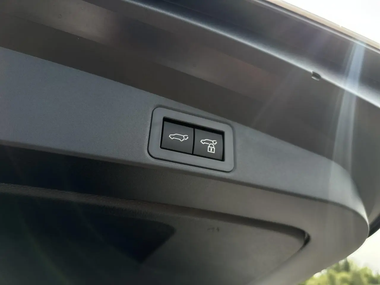 Gros plan sur les boutons d'ouverture et de verrouillage électrique du hayon du coffre d'une Toyota Corolla Touring Sport blanc neige.