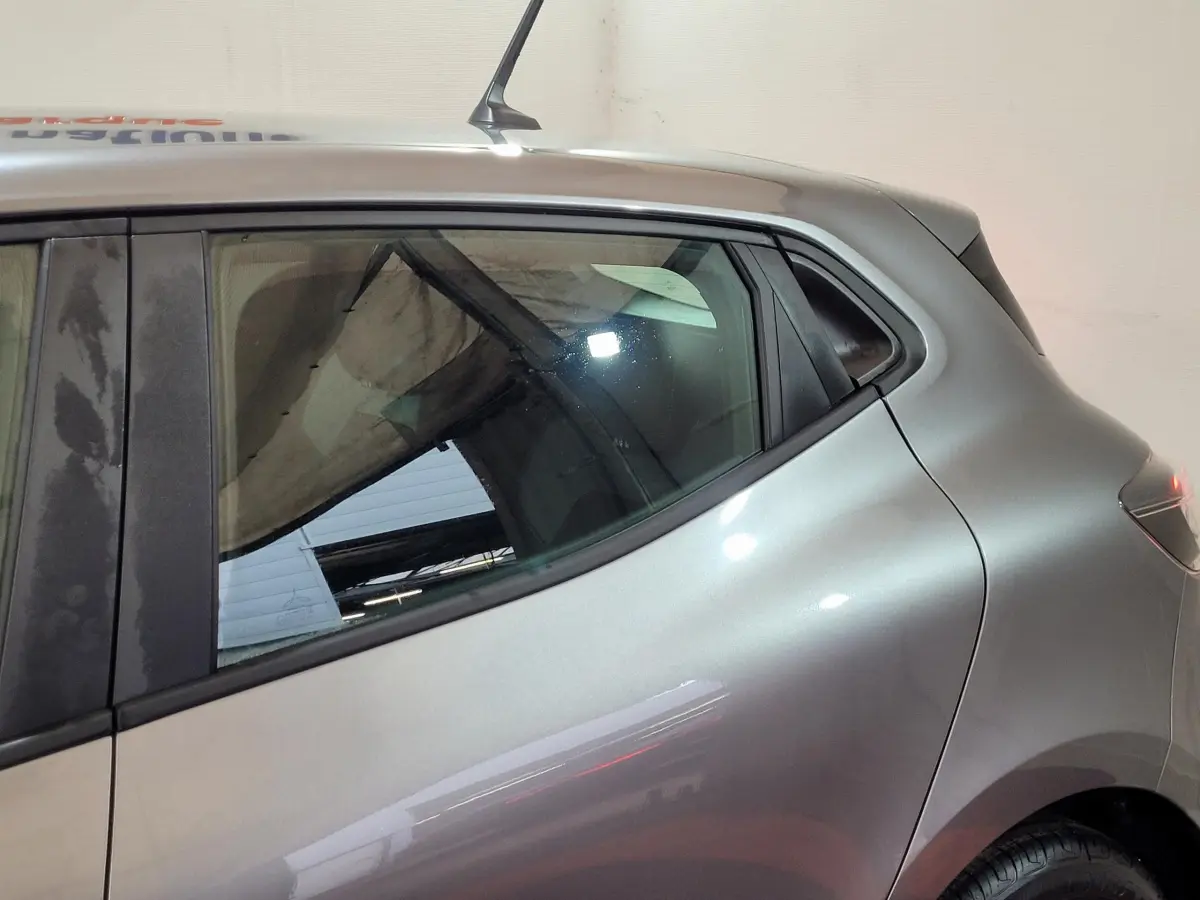 Vue latérale côté gauche sur l'arrière d'une Renault Clio gris foncé avec vitres teintées et antenne de toit.