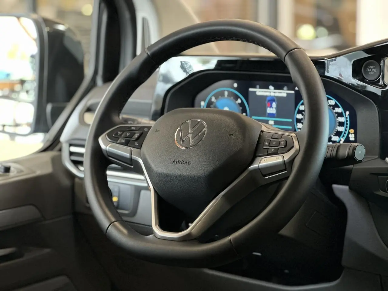 Vue rapprochée du volant multifonction noir du Volkswagen Transporter T7 avec tableau de bord digital en arrière-plan.