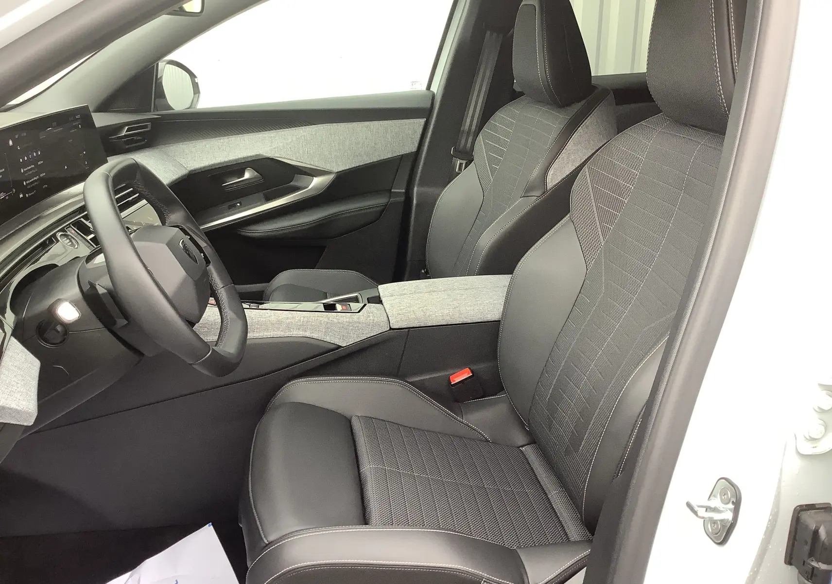 Vue intérieure côté conducteur du Peugeot 3008 Hybrid 2024, sièges noirs en cuir et tissu avec console centrale gris clair.