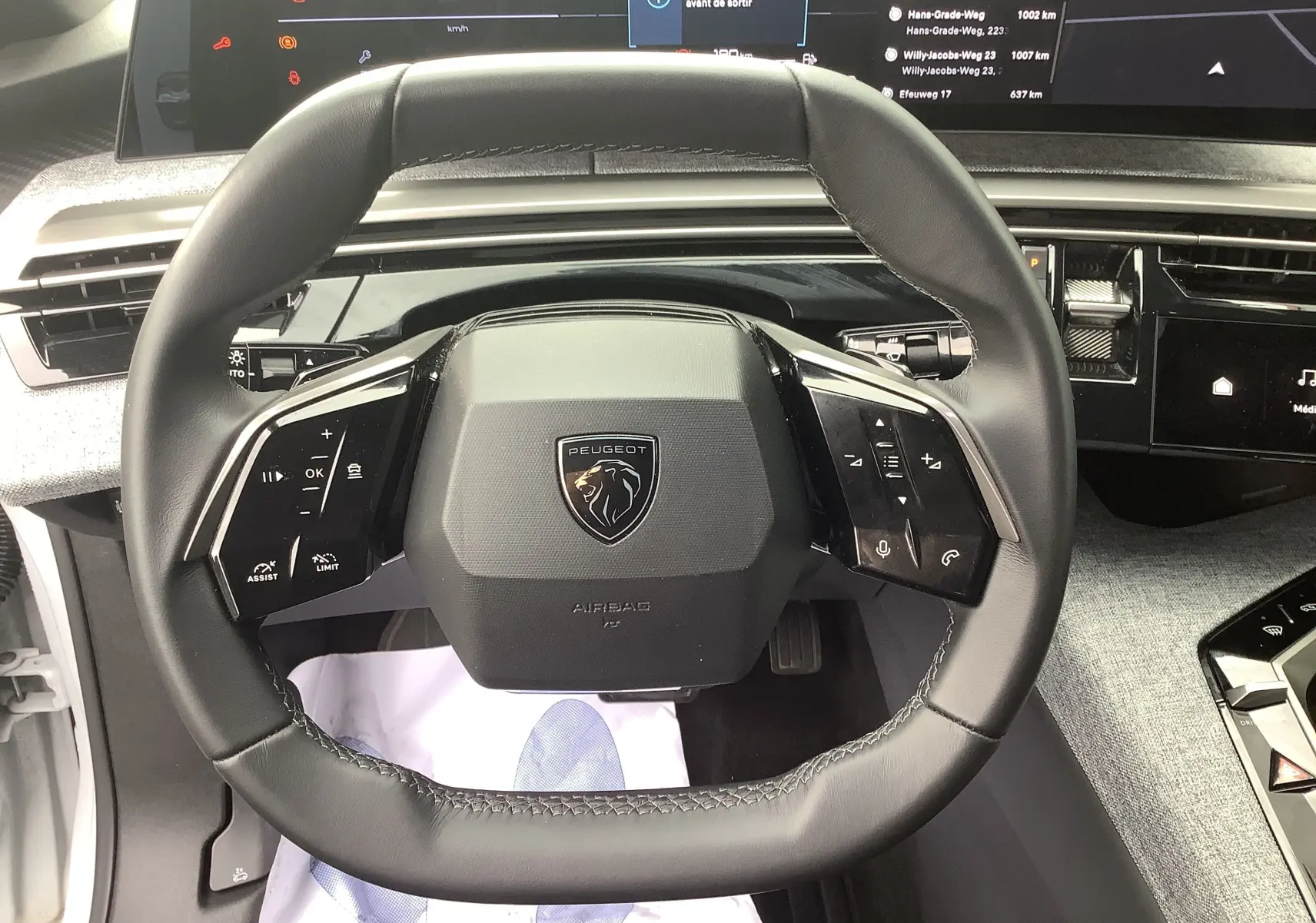 Vue rapprochée du volant cuir noir de la Peugeot 3008 Hybrid 2024 avec commandes intégrées et tableau de bord digital.