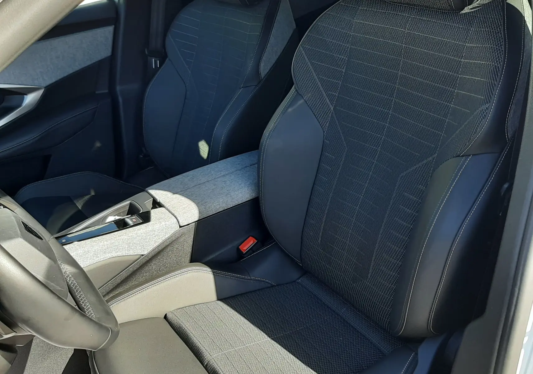 Vue intérieure côté conducteur du Peugeot 3008 HYBRID 145 avec sièges noirs tissu et cuir, console centrale gris clair.