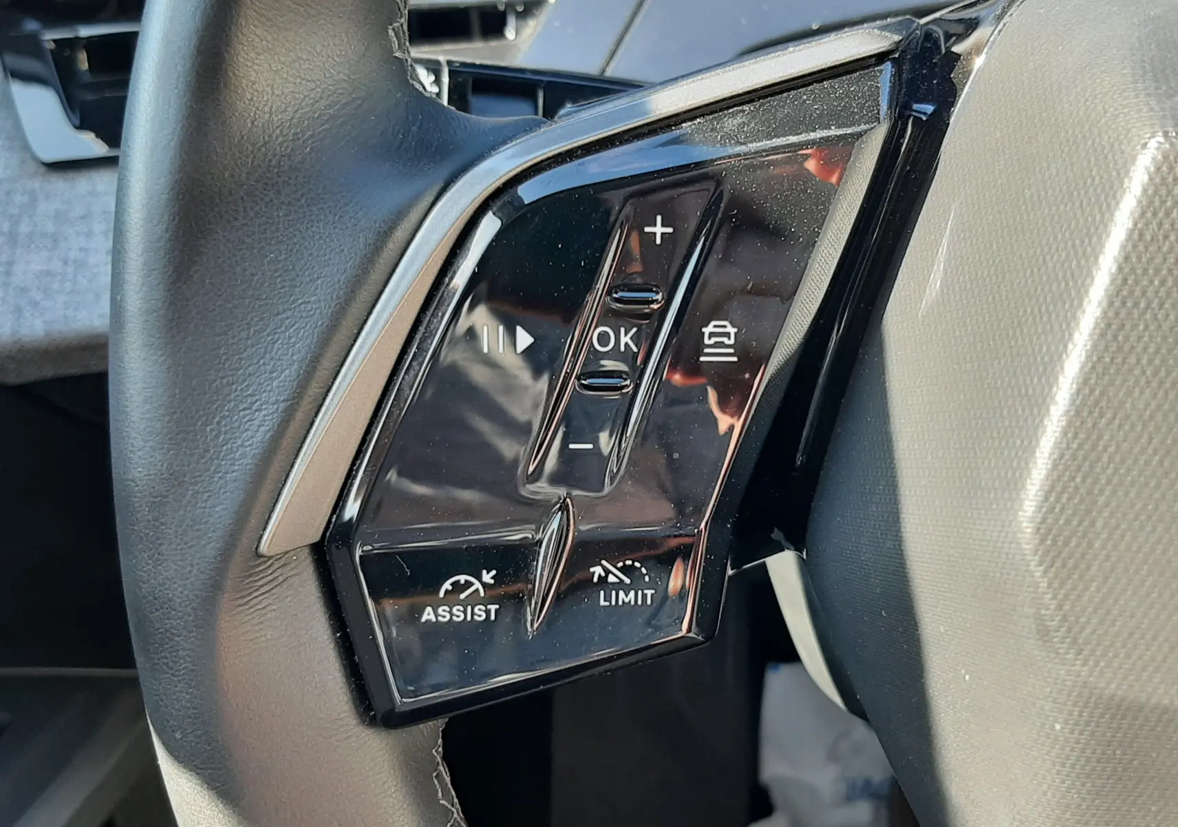 Gros plan sur les commandes noires du volant côté gauche du Peugeot 3008 Hybrid 145 blanc Okenite 2024.
