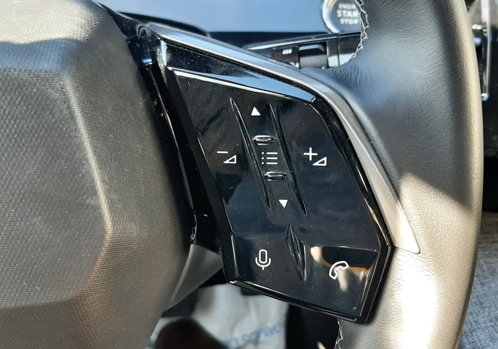 Gros plan sur les commandes noires du volant cuir du Peugeot 3008 Hybrid 2024, avec bouton micro et téléphone visible.