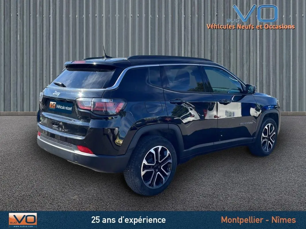 Jeep Compass noir en 3/4 arrière droit, avec barres de toit et jantes 18 pouces visibles sur sol bitumé.