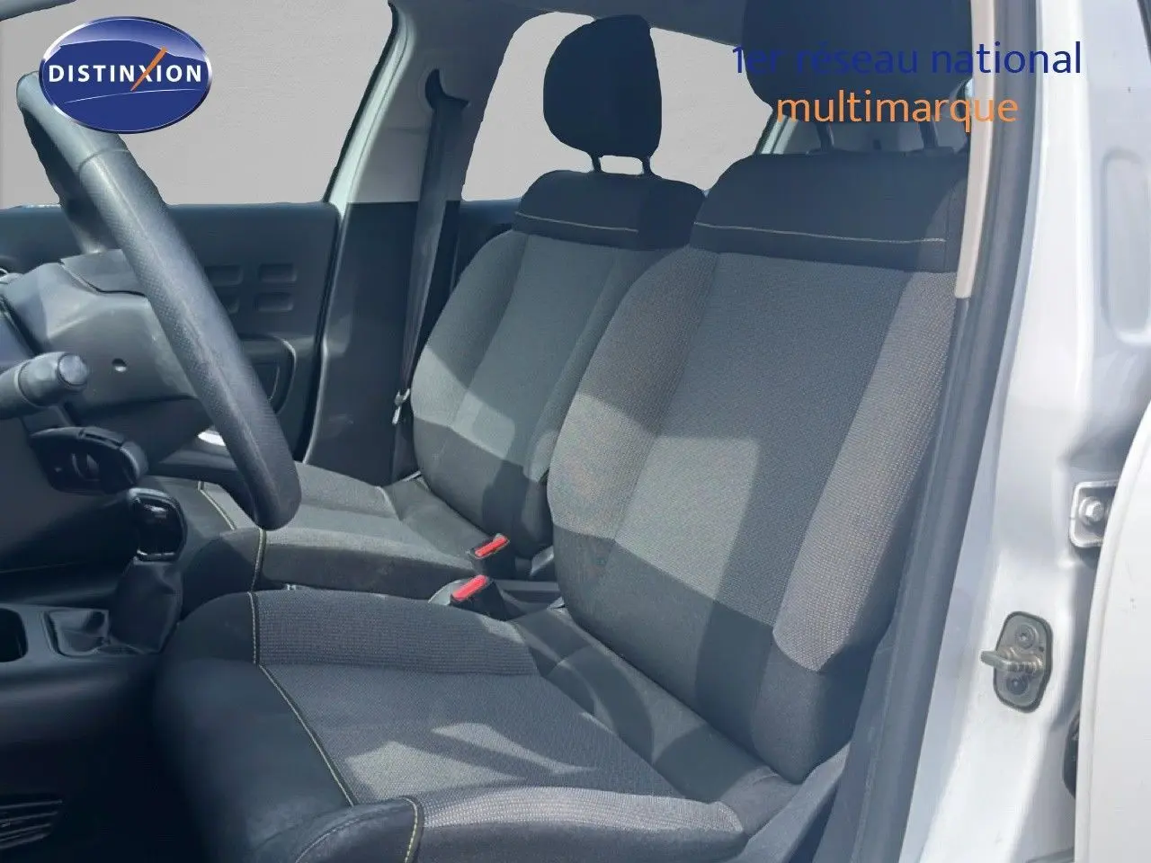Vue intérieure côté conducteur d'une Citroën C3 blanche 2018, sièges tissu gris avec surpiqûres contrastantes.