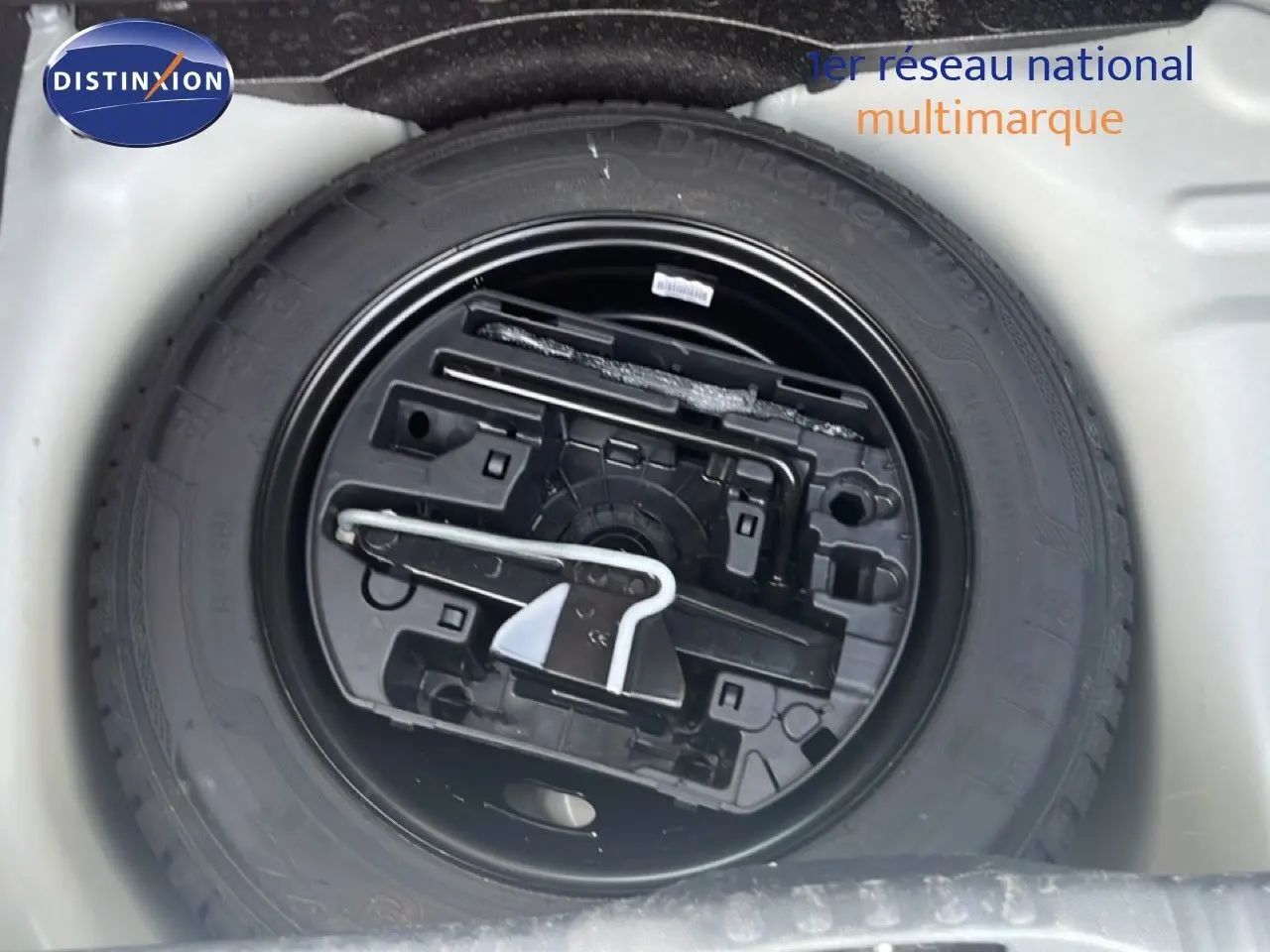 Vue rapprochée de la roue de secours noire et de son rangement dans le coffre d'une Citroën C3 blanche.
