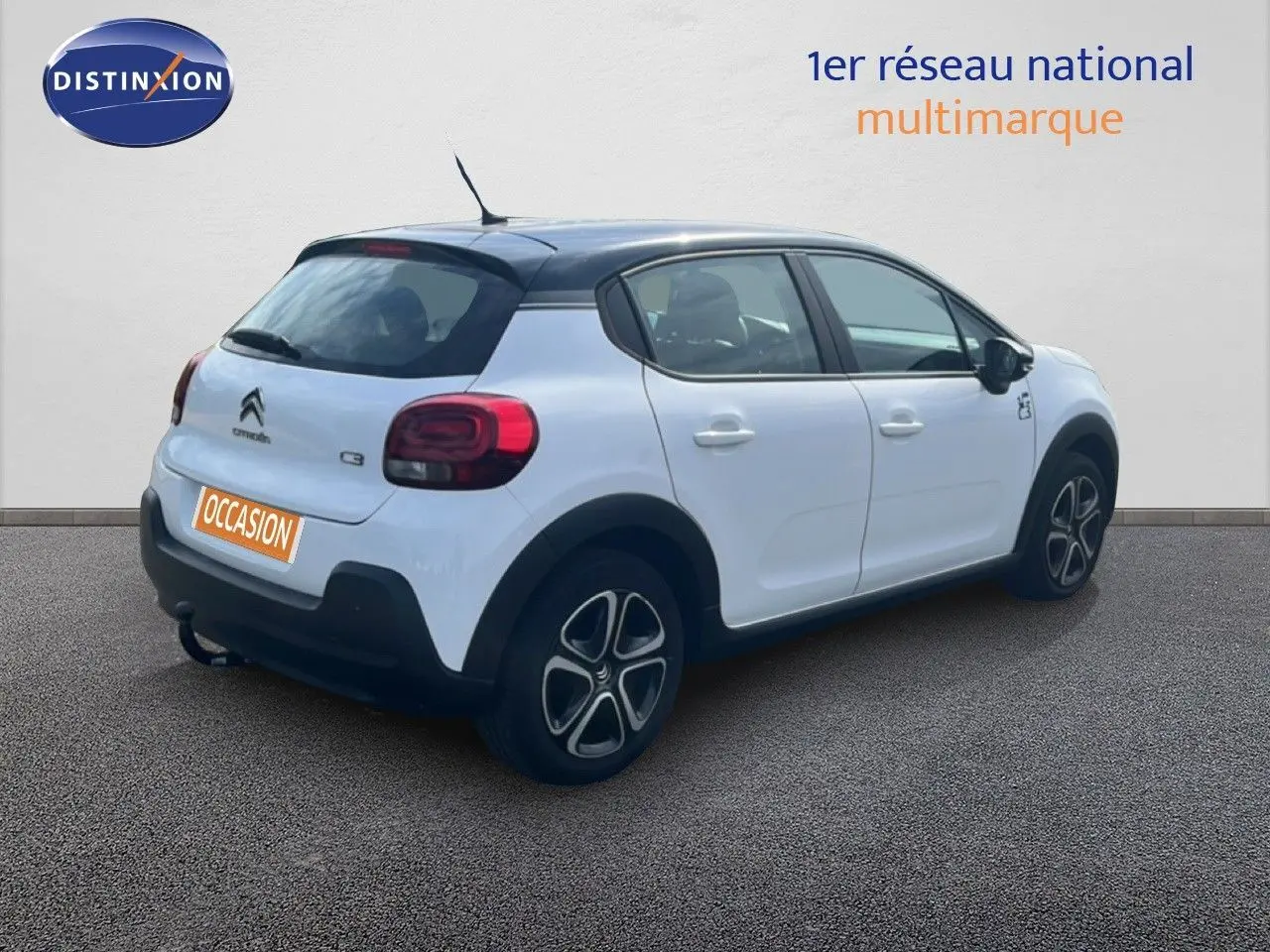 Citroën C3 blanc en 3/4 arrière droit avec toit noir et jantes distinctives, stationnée sur sol gris.