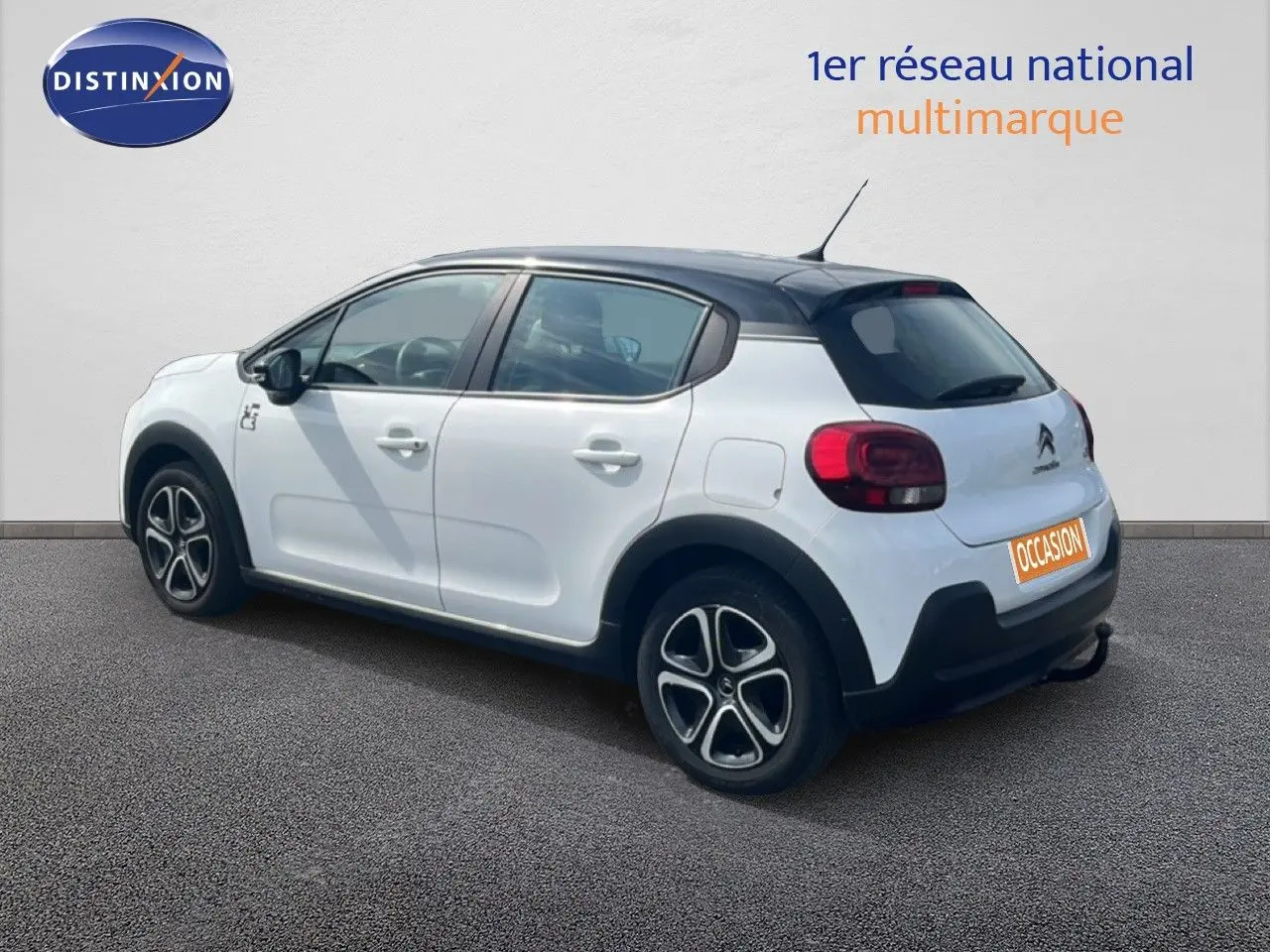 Vue 3/4 arrière droite d'une Citroën C3 blanche 2018 avec toit noir et jantes distinctives, en extérieur sur sol gris.