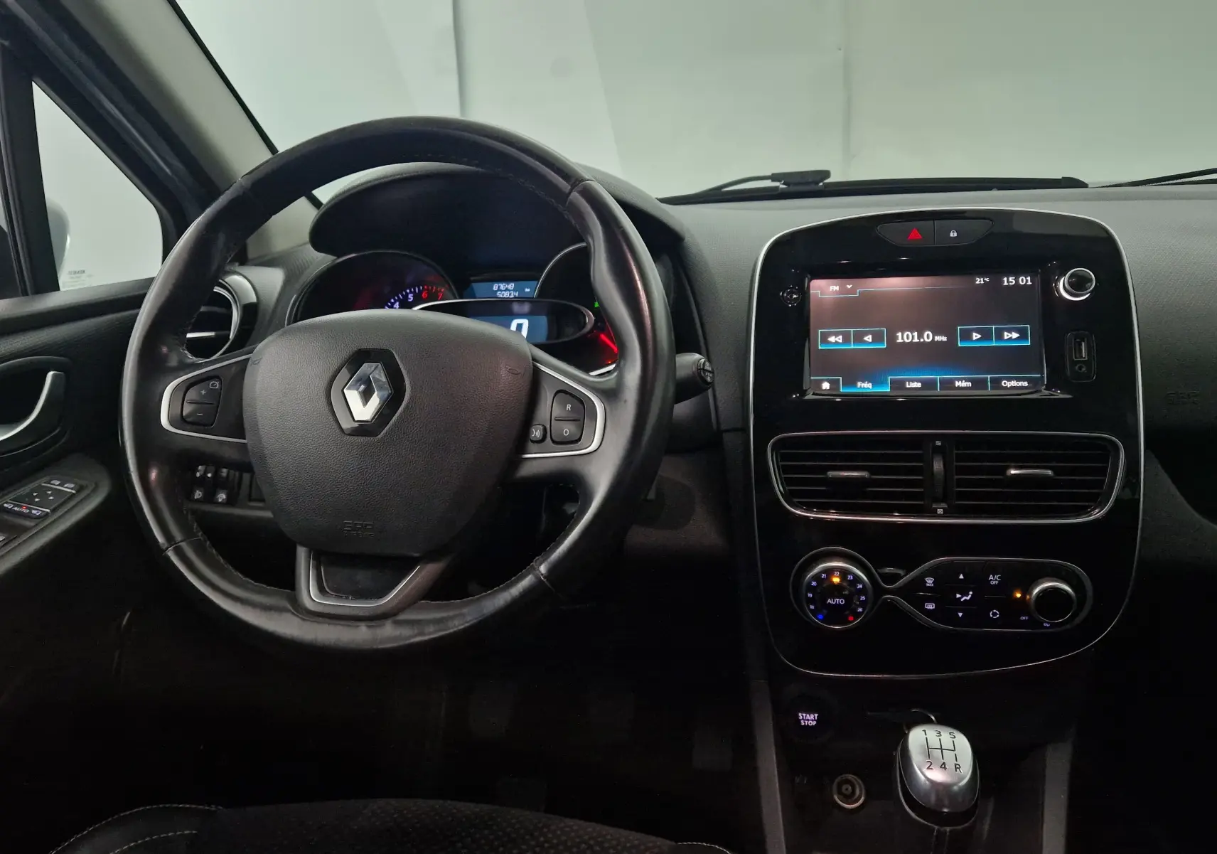 Vue intérieure du tableau de bord et volant cuir de la Renault Clio IV gris clair métal avec écran tactile et boîte manuelle.
