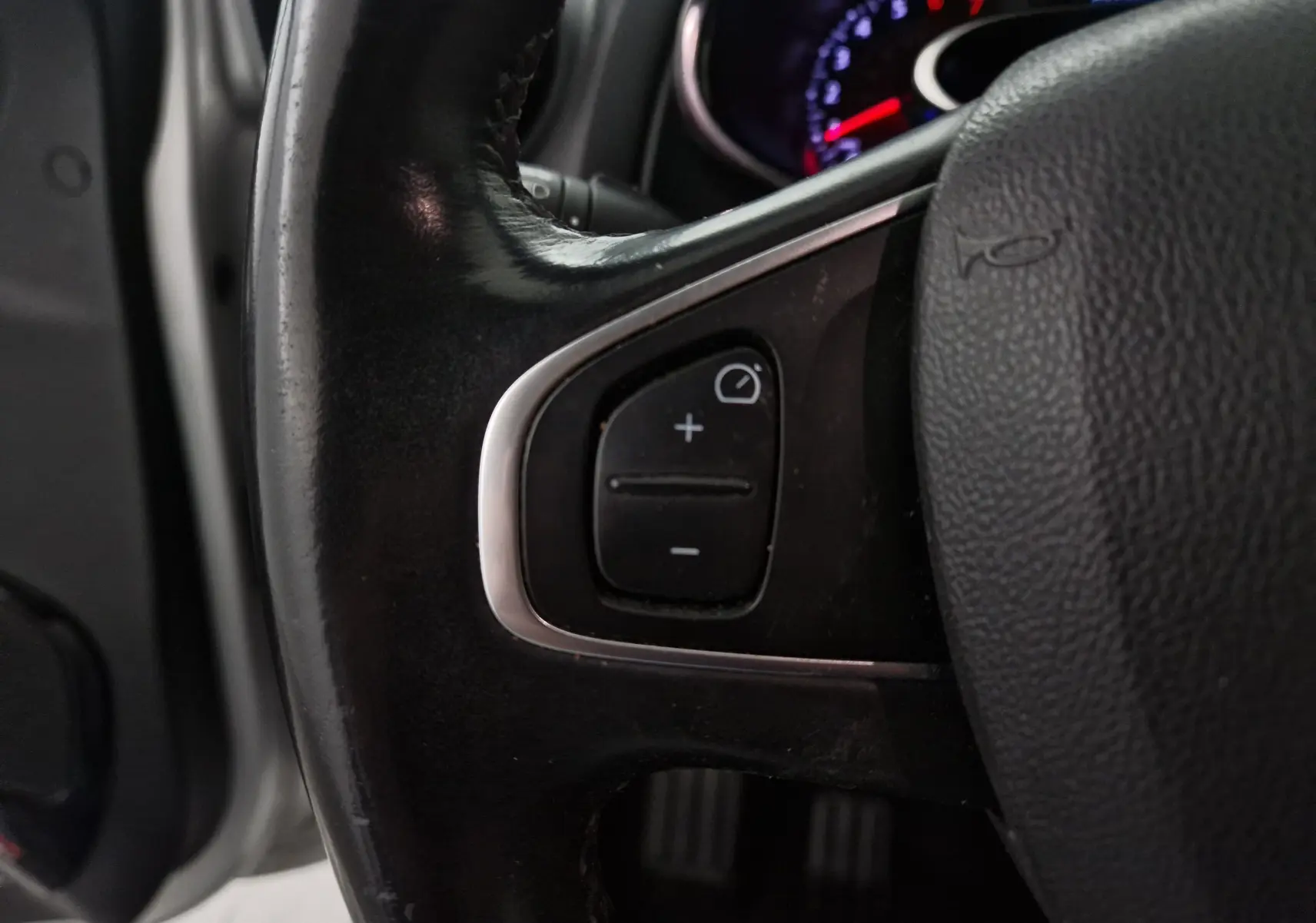 Gros plan sur le côté gauche du volant en cuir noir d'une Renault Clio IV gris clair, avec commandes de régulateur de vitesse visibles.