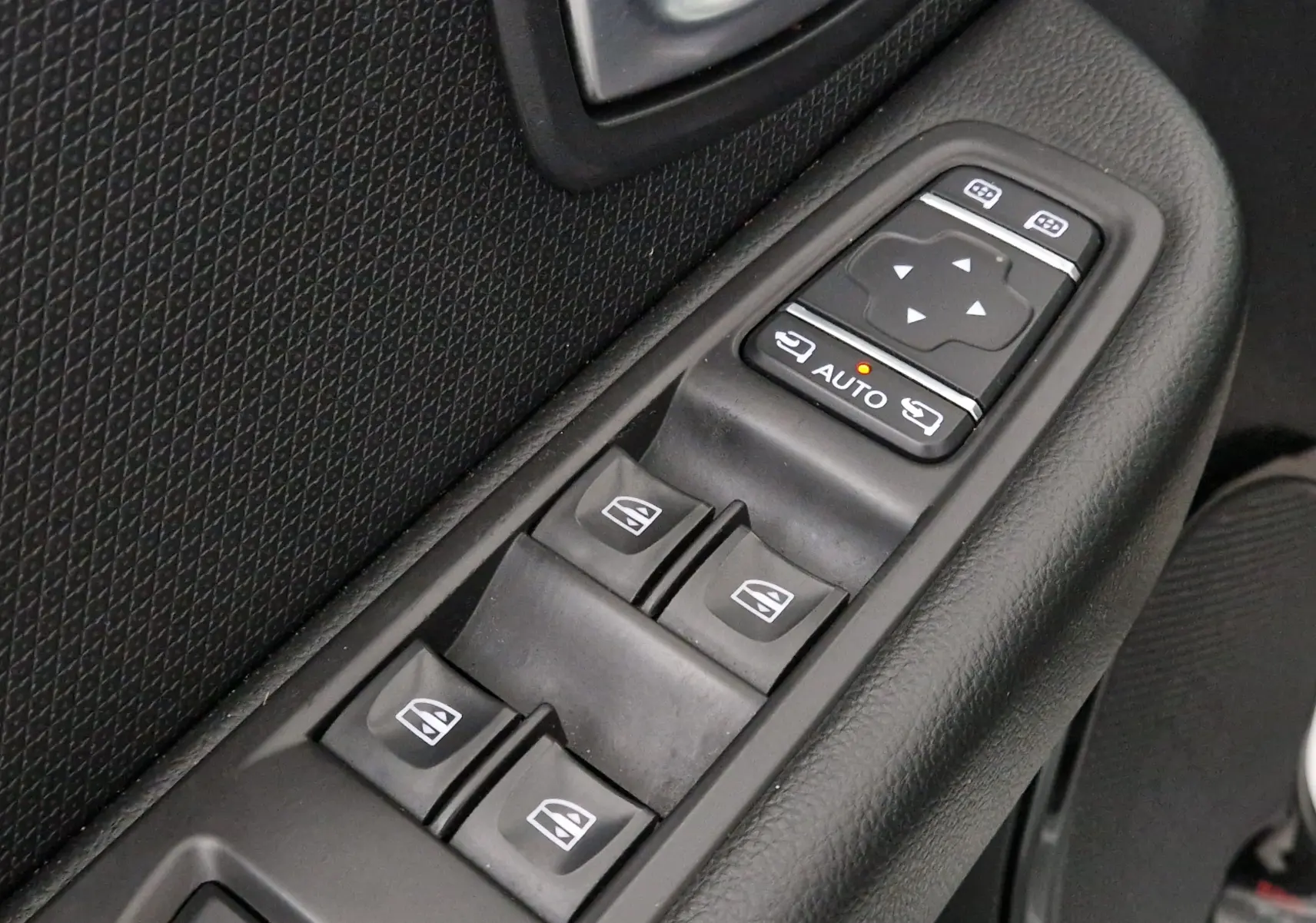 Gros plan sur les commandes de lève-vitres et réglage des rétroviseurs côté conducteur d'une Renault Clio IV gris clair.