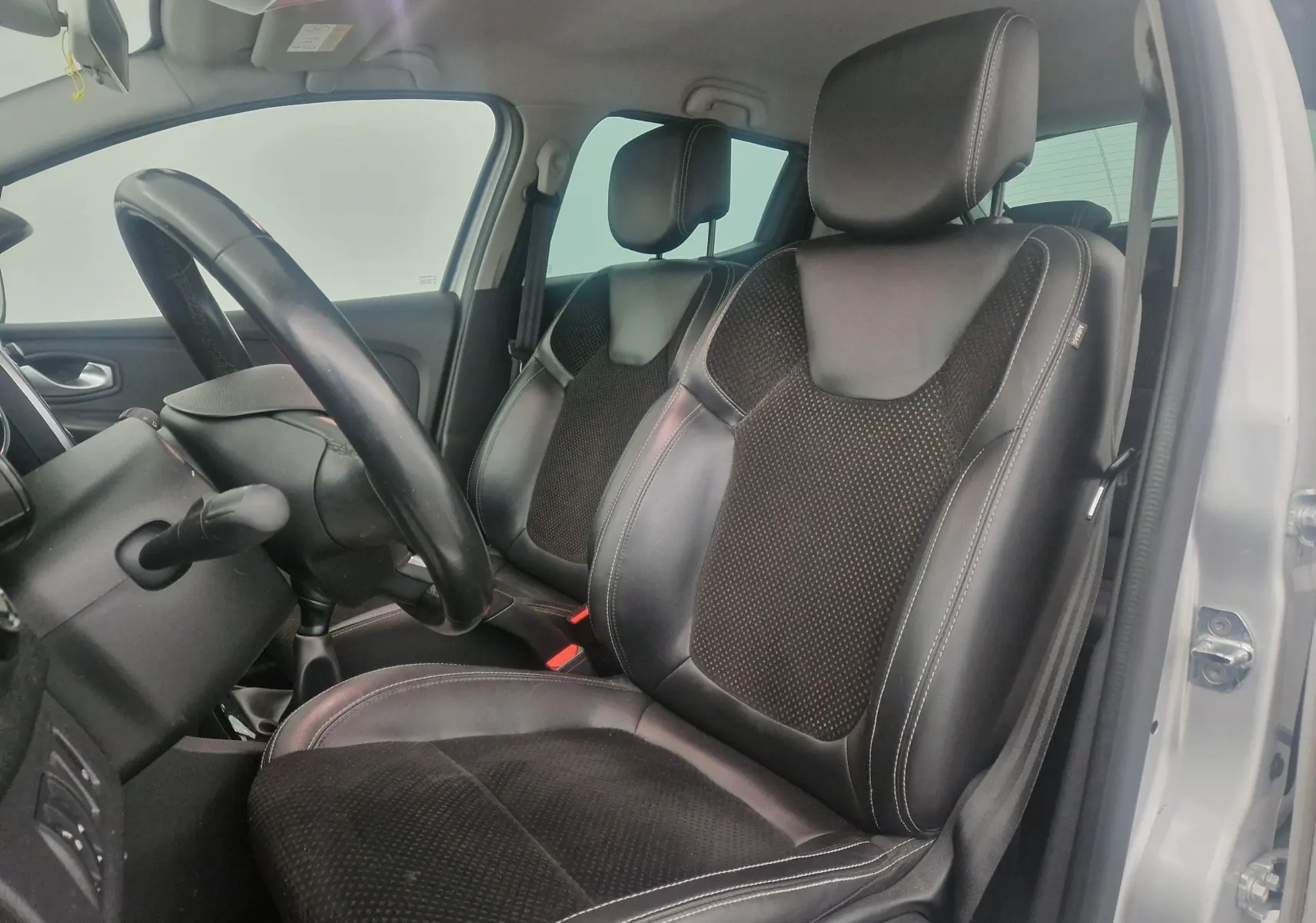 Vue intérieure côté conducteur de la Renault Clio IV 2018, sièges en cuir noir avec surpiqûres blanches, volant visible.