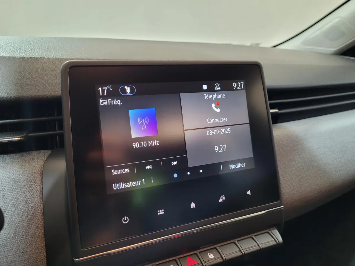 Écran tactile central de la Renault Clio gris foncé affichant radio et téléphone, vue intérieure côté passager.