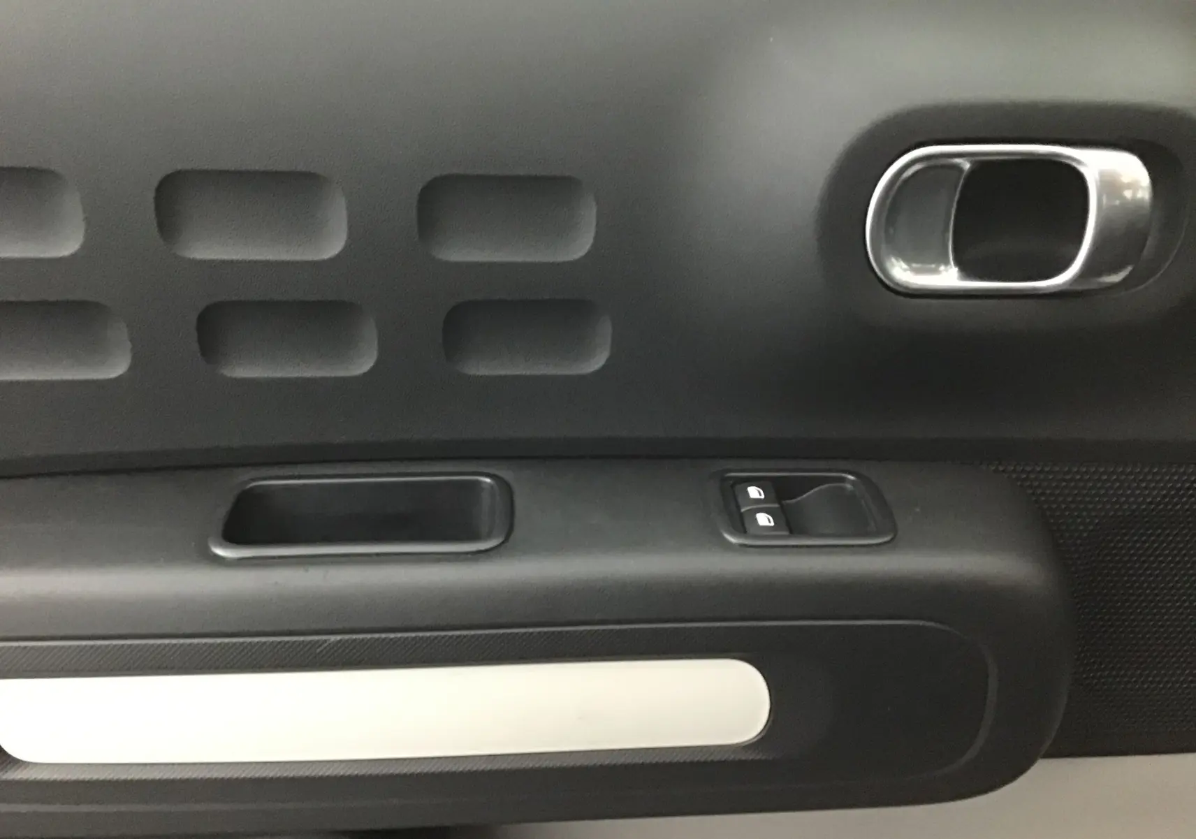 Détail de la porte côté gauche de la Citroën C3 2022 gris platinium, montrant la poignée intérieure et les commandes de vitres.