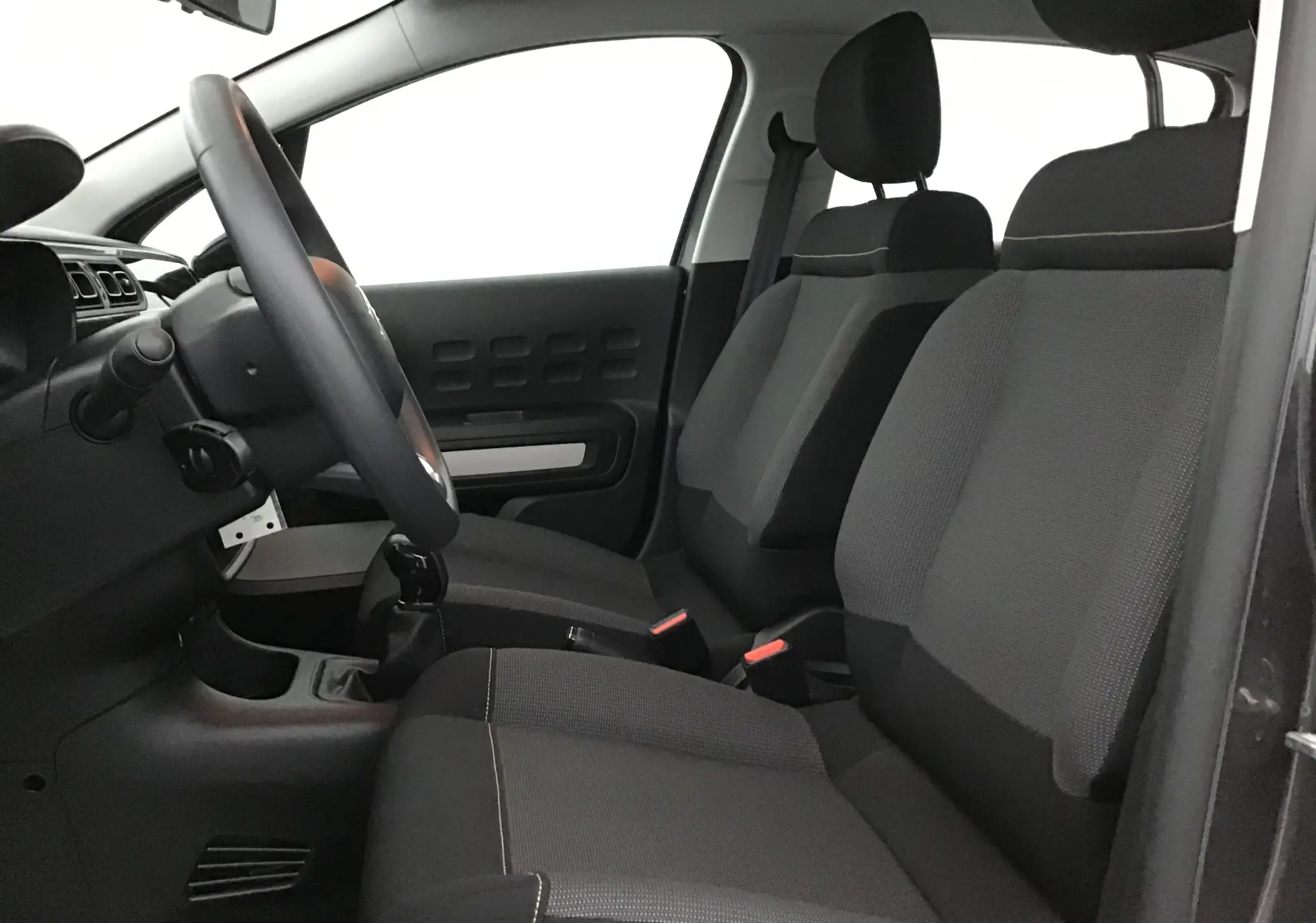 Vue intérieure côté conducteur de la Citroën C3 2022, sièges tissu gris et volant avec levier de vitesses manuel.