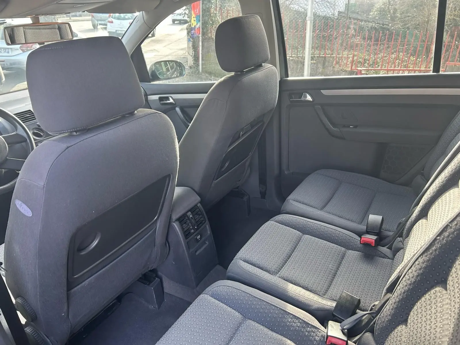 Vue intérieure arrière du Volkswagen Touran gris 2004, montrant les sièges tissu et la console centrale avec aérateurs.