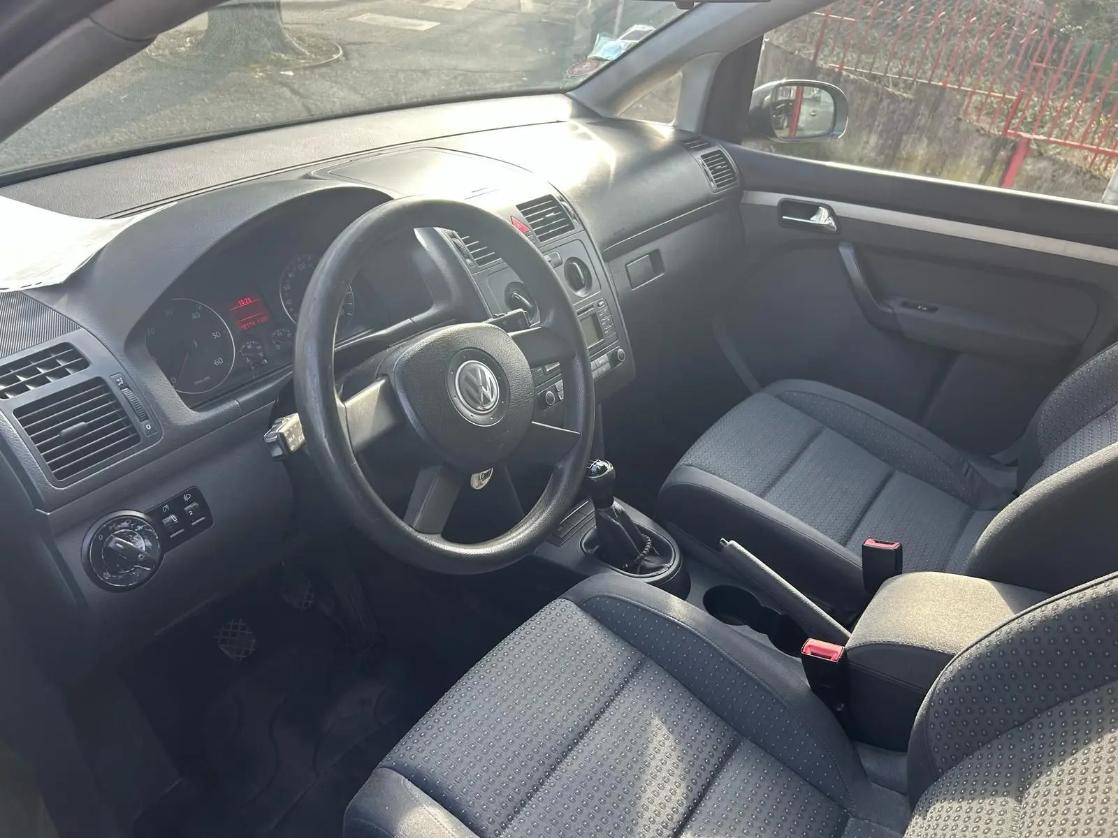 Intérieur du Volkswagen Touran 2004 vu côté conducteur, volant cuir, sièges tissu gris et boîte manuelle.