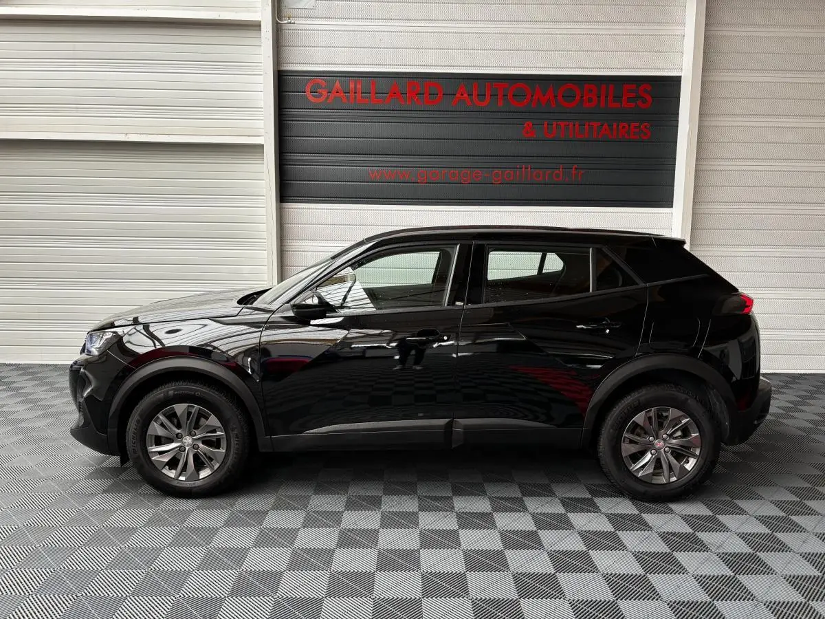 Profil côté gauche d'un Peugeot 2008 noir 2021 garé en intérieur sur sol à damier devant un mur blanc.