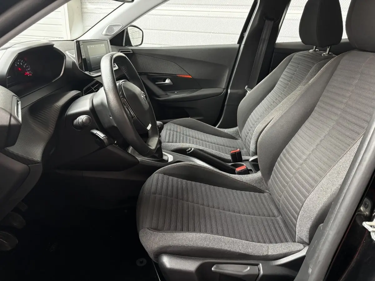 Vue intérieure côté conducteur de la Peugeot 2008 noire 2021, avec sièges tissu gris et tableau de bord moderne.