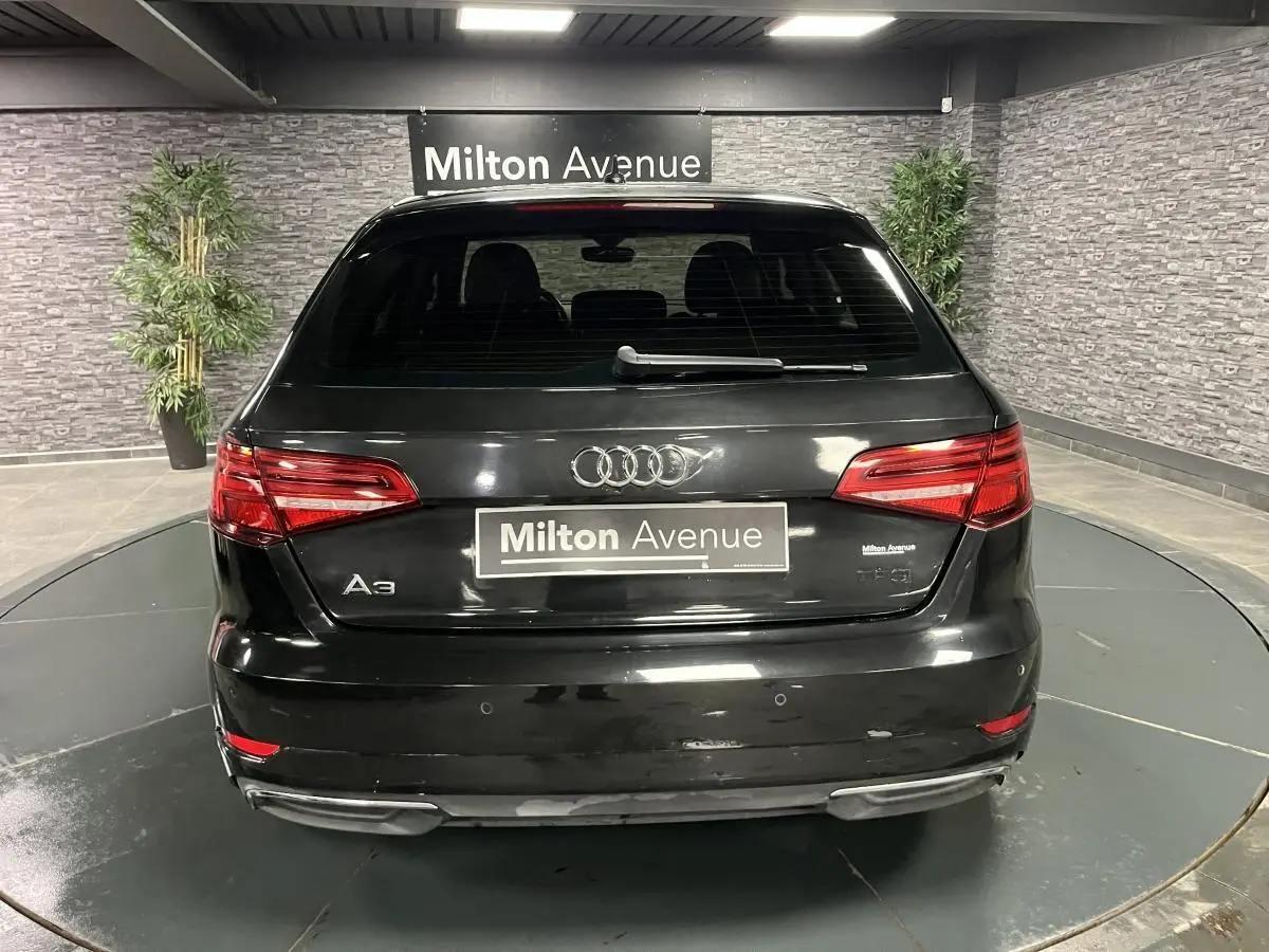 Vue arrière d'une Audi A3 noire avec logo et plaques Milton Avenue dans un showroom intérieur.