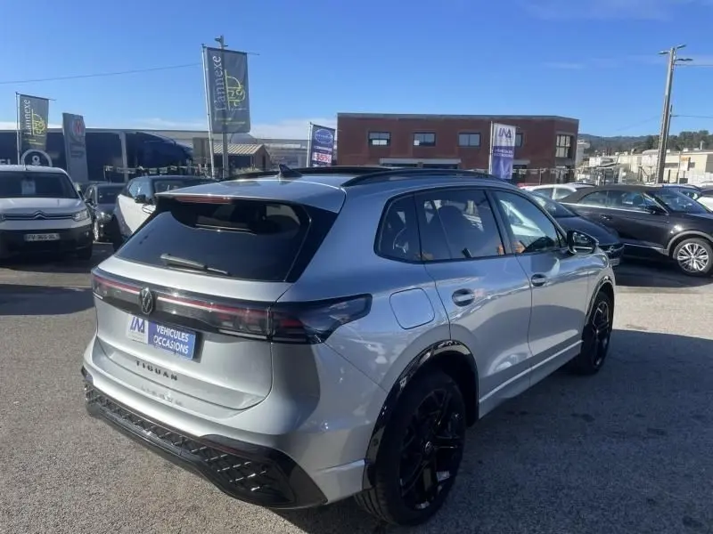 Vue 3/4 arrière droite d'un Volkswagen Tiguan gris métal 2025, version R-line avec jantes noires et toit panoramique.