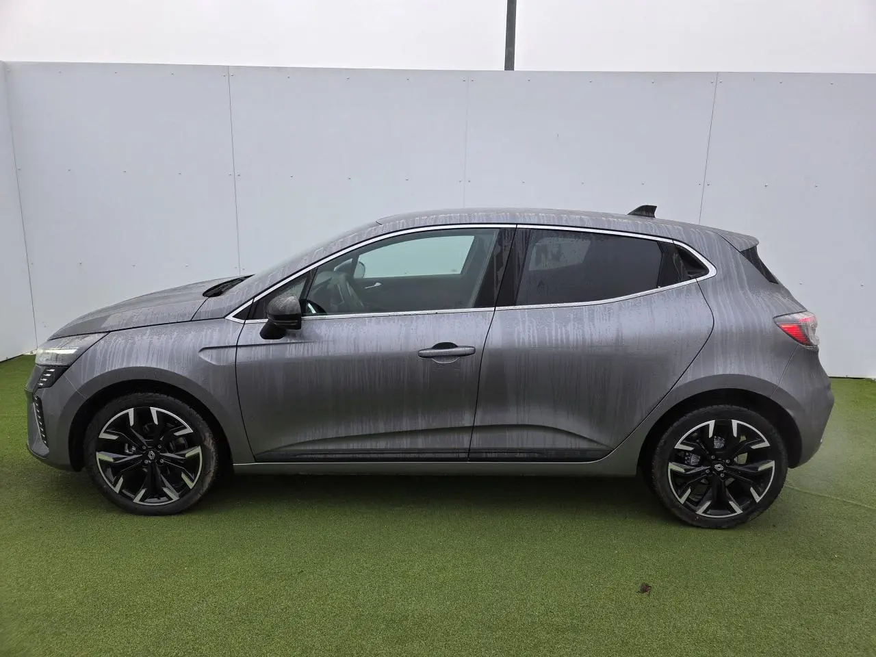 Profil droit d'une Renault Clio 2025 gris schiste métal avec jantes alliage noires et contour de vitres chromé.