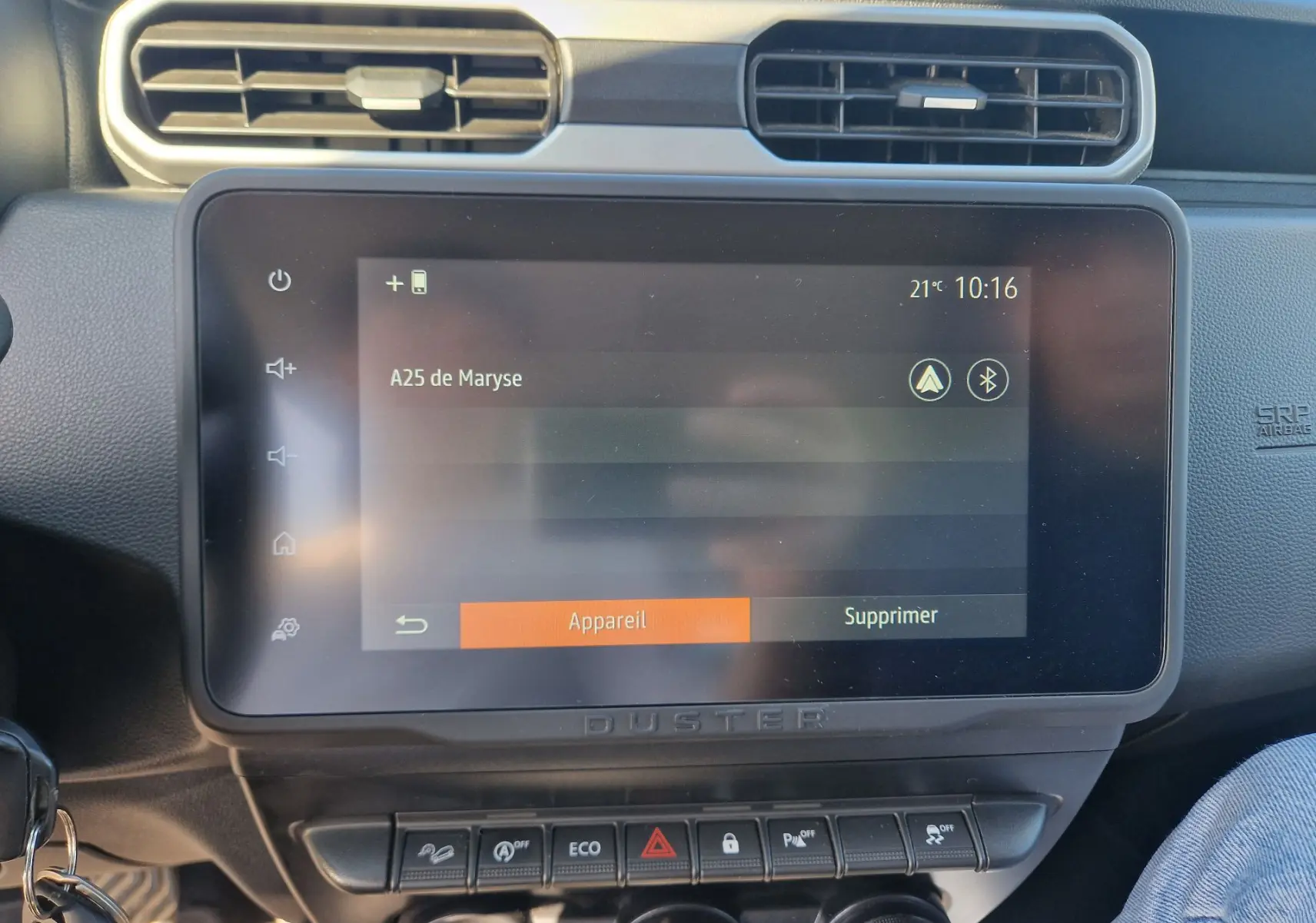 Écran tactile central du tableau de bord du Dacia Duster 2024 blanc, avec commandes et ventilation visibles.