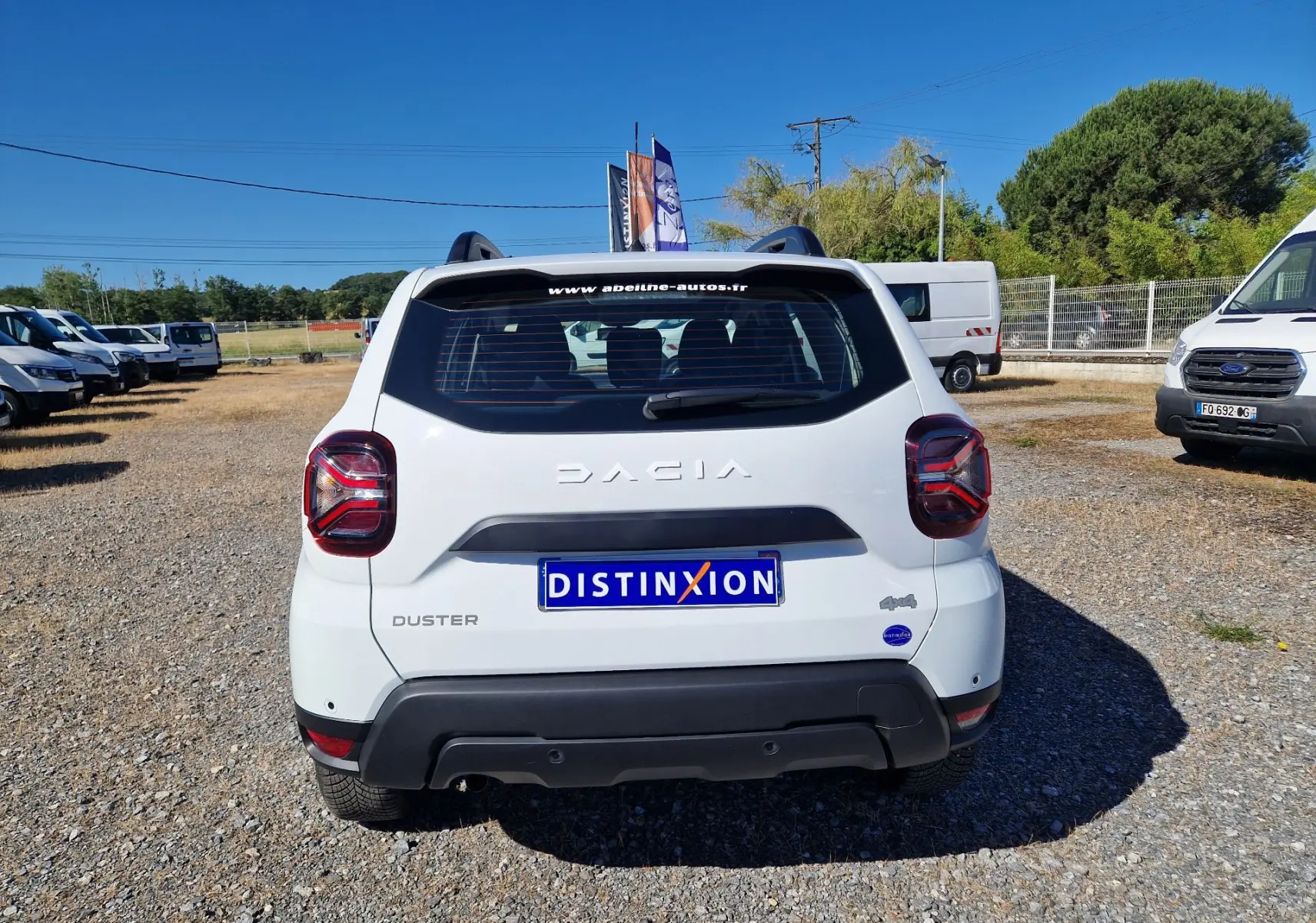 Vue arrière d'un Dacia Duster blanc 4x4 2024, avec logo et plaque Distinxion visible sur un terrain extérieur.